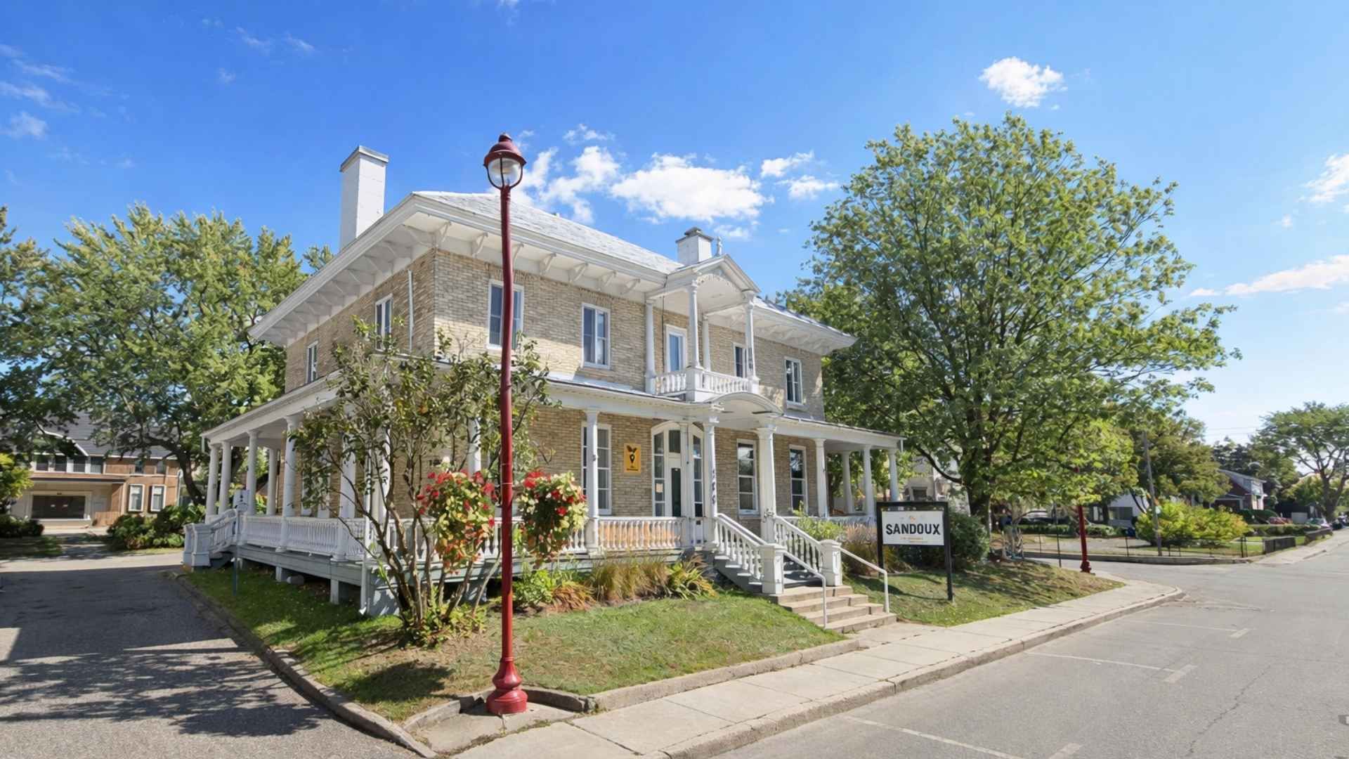 Restaurant de deux étages avec une barrière blanche qui l'entoure, situé sur un terrain d'angle sous un ciel bleu.
