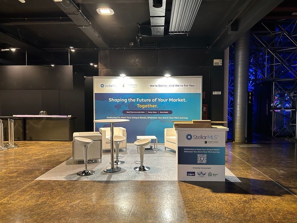 Event booth with a banner, chairs, and tables on a patterned floor.