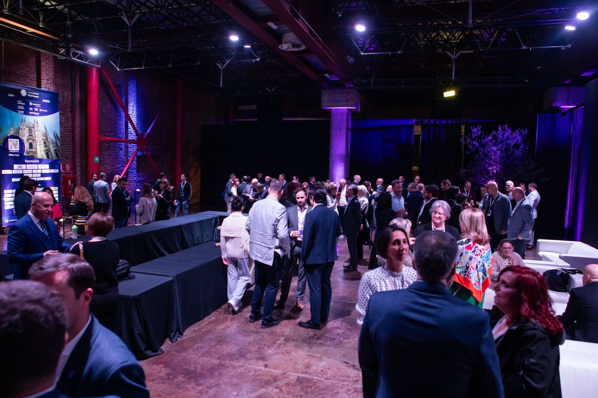 Large room with many people. Dark lighting with colorful accents.