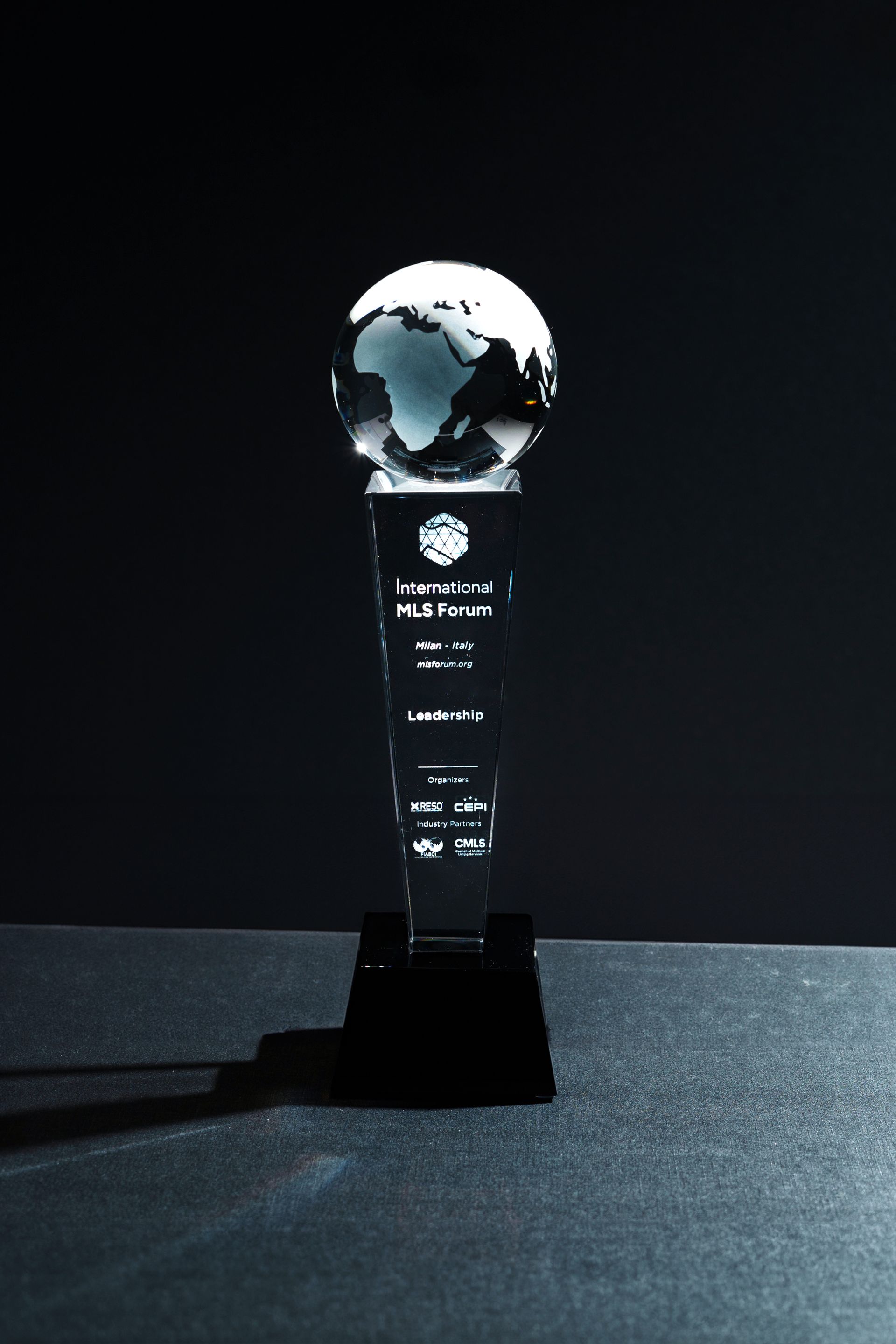 Crystal trophy with globe on top, black base, text on column, dark background.