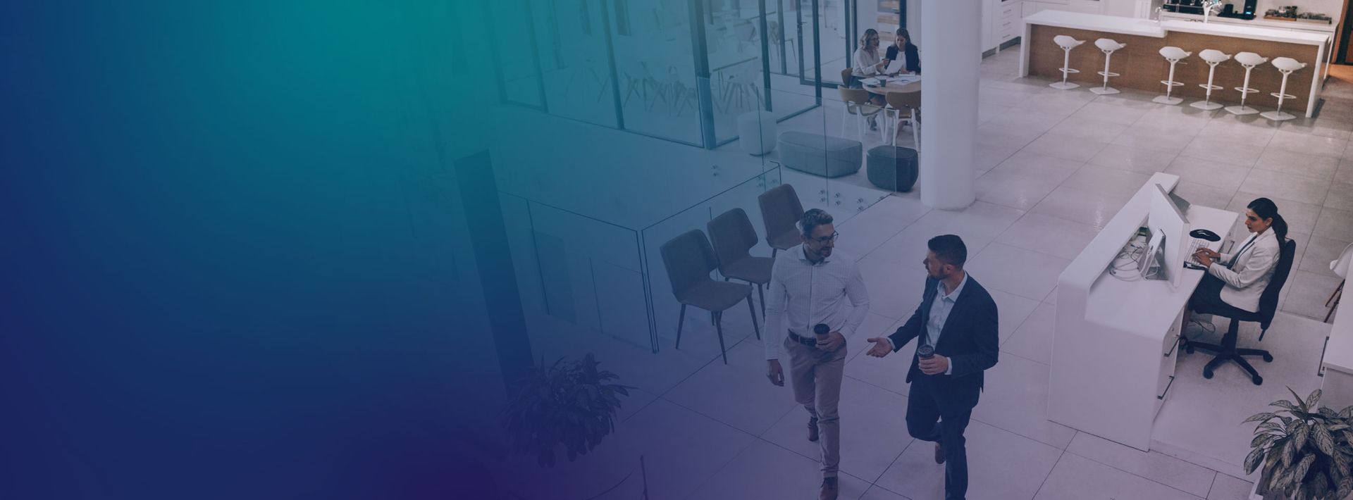 Two professionals walk and talk across a modern, bright office lobby, with a reception area in the background.
