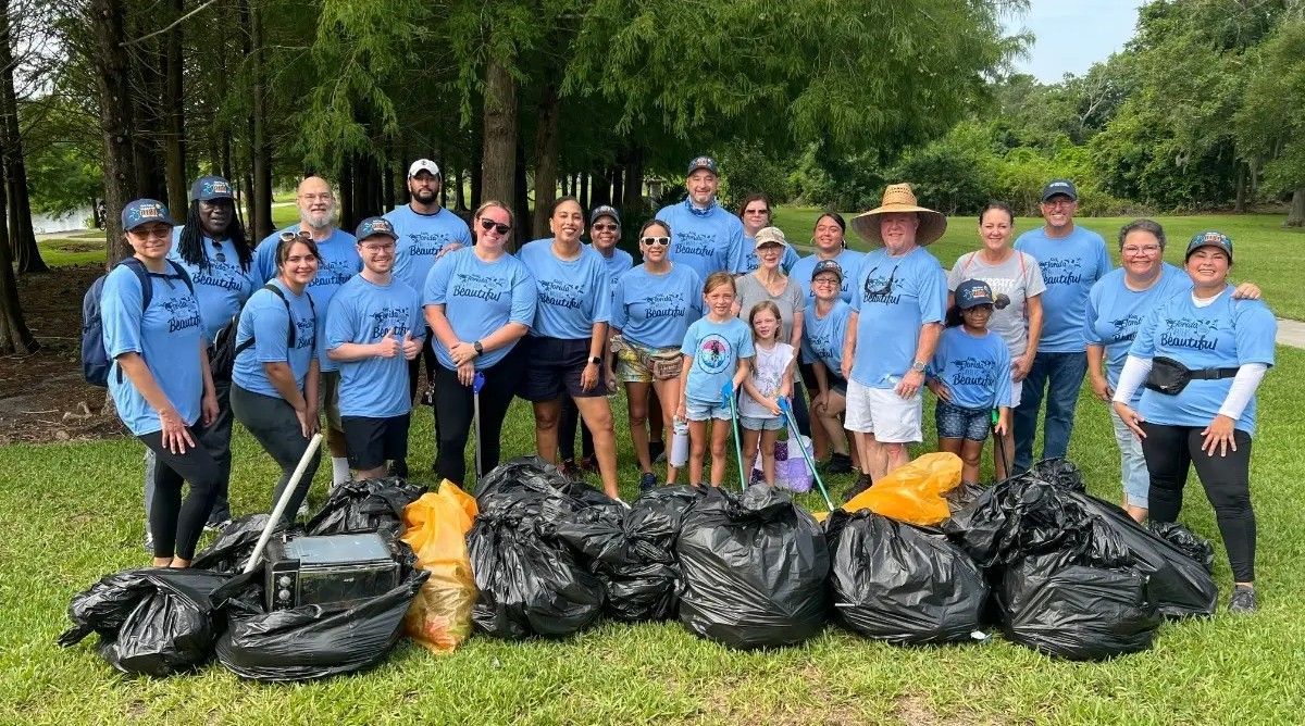 Group of people in blue shirts stand with trash bags in a park, smiling.