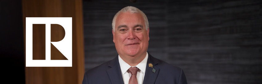 A man in a suit and tie is standing in front of a brick wall.