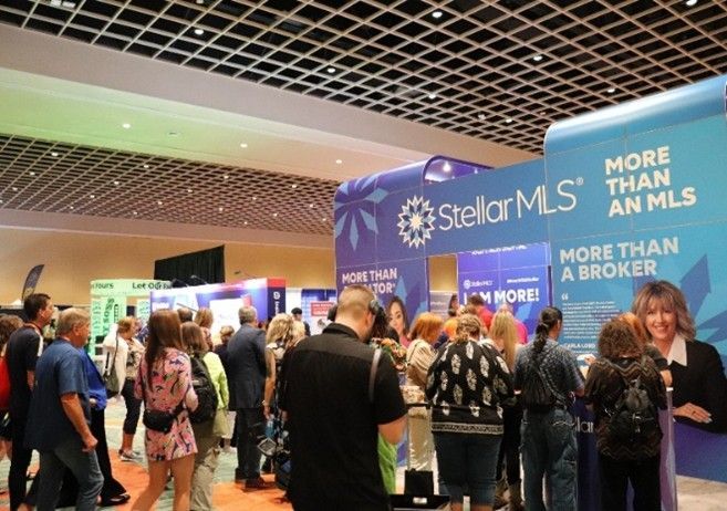 Crowd at StellarMLS booth at a conference, people standing, blue and white branding, event setting.