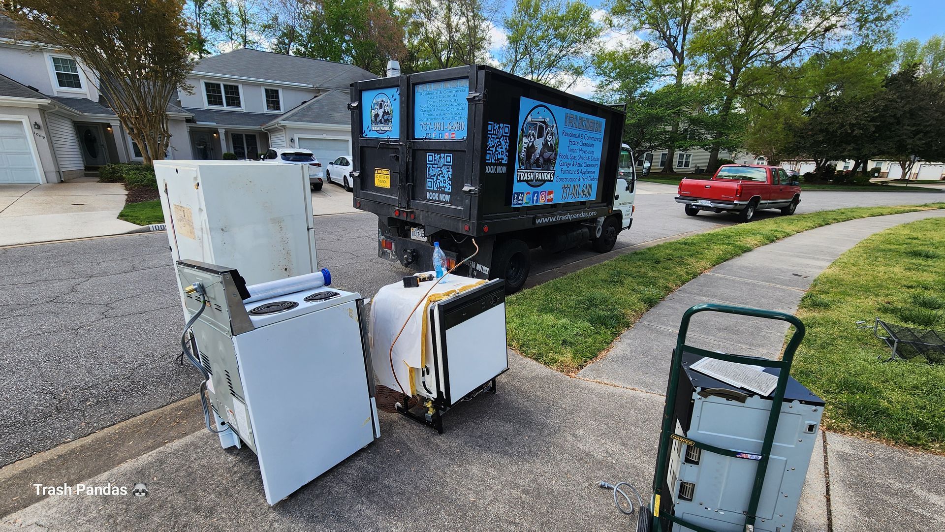 A dumpster truck filled with appliances is parked on the side of the road.