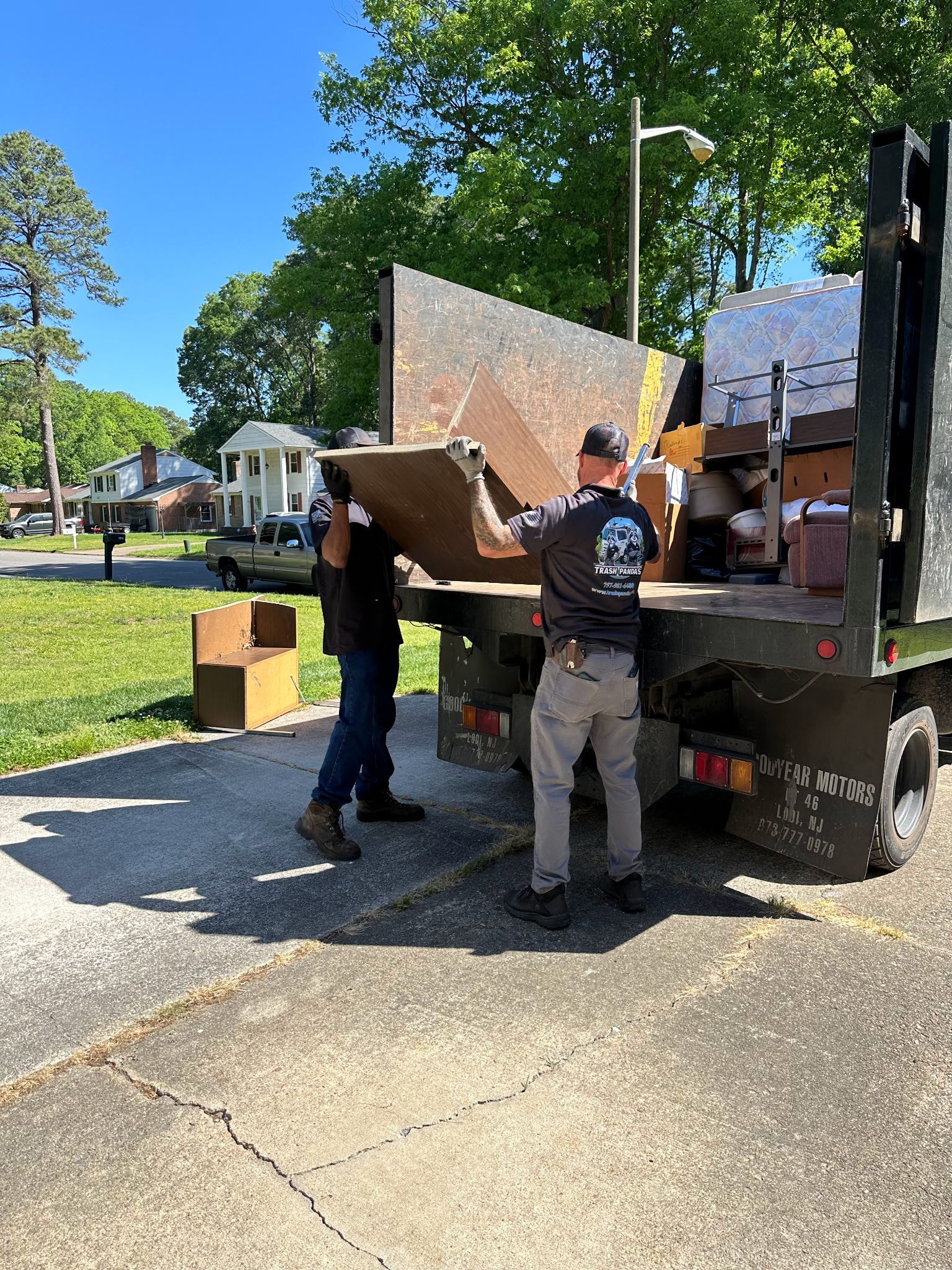 Two men are loading a large piece of wood into a dumpster.