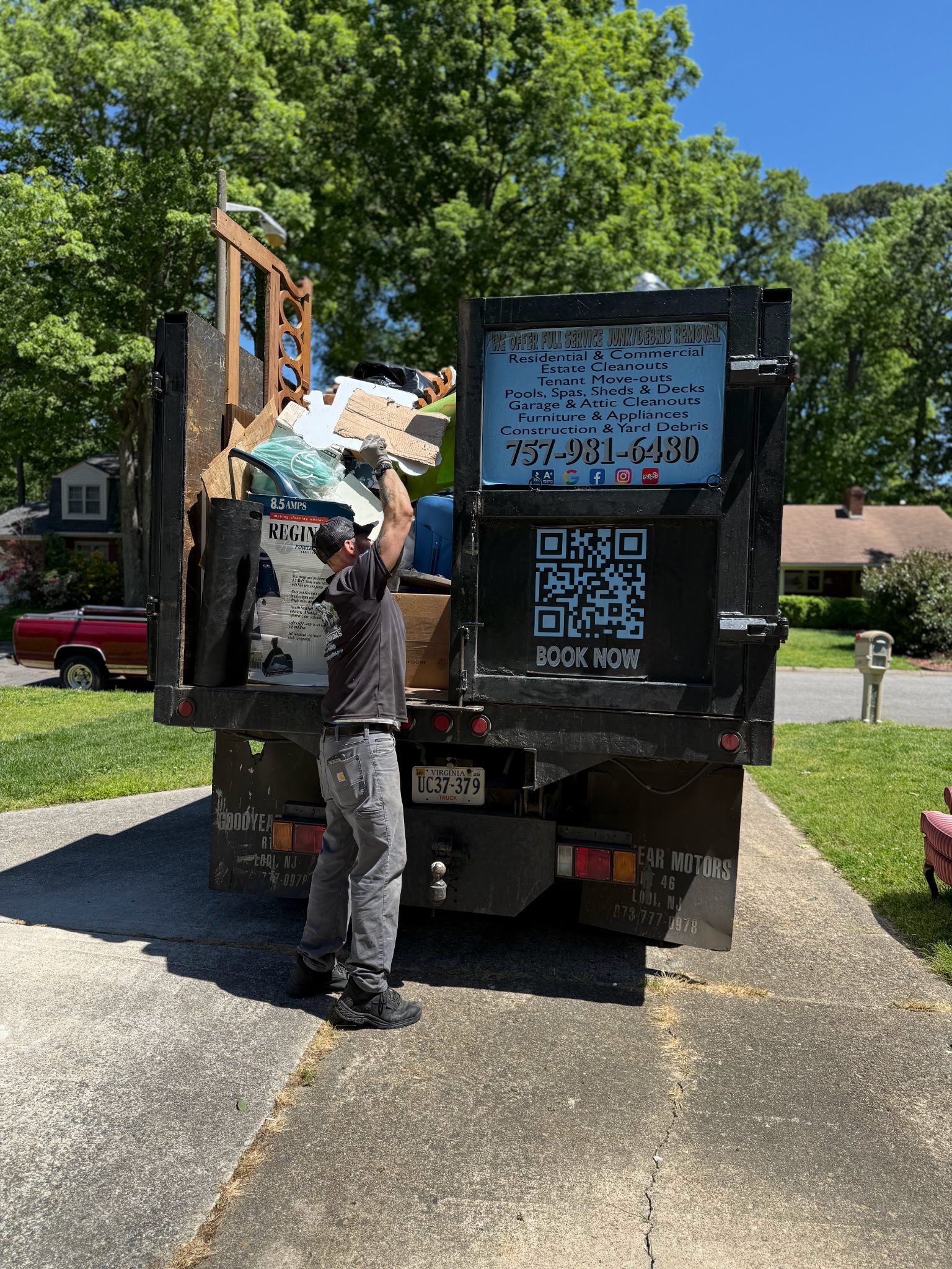 A man is standing in front of a dumpster filled with junk.