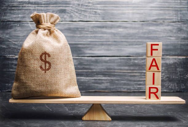 A bag of money is sitting on a wooden scale next to a block that says fair.