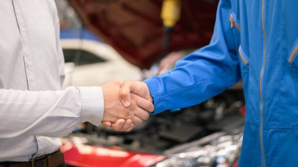 A man and a mechanic are shaking hands in front of a car.