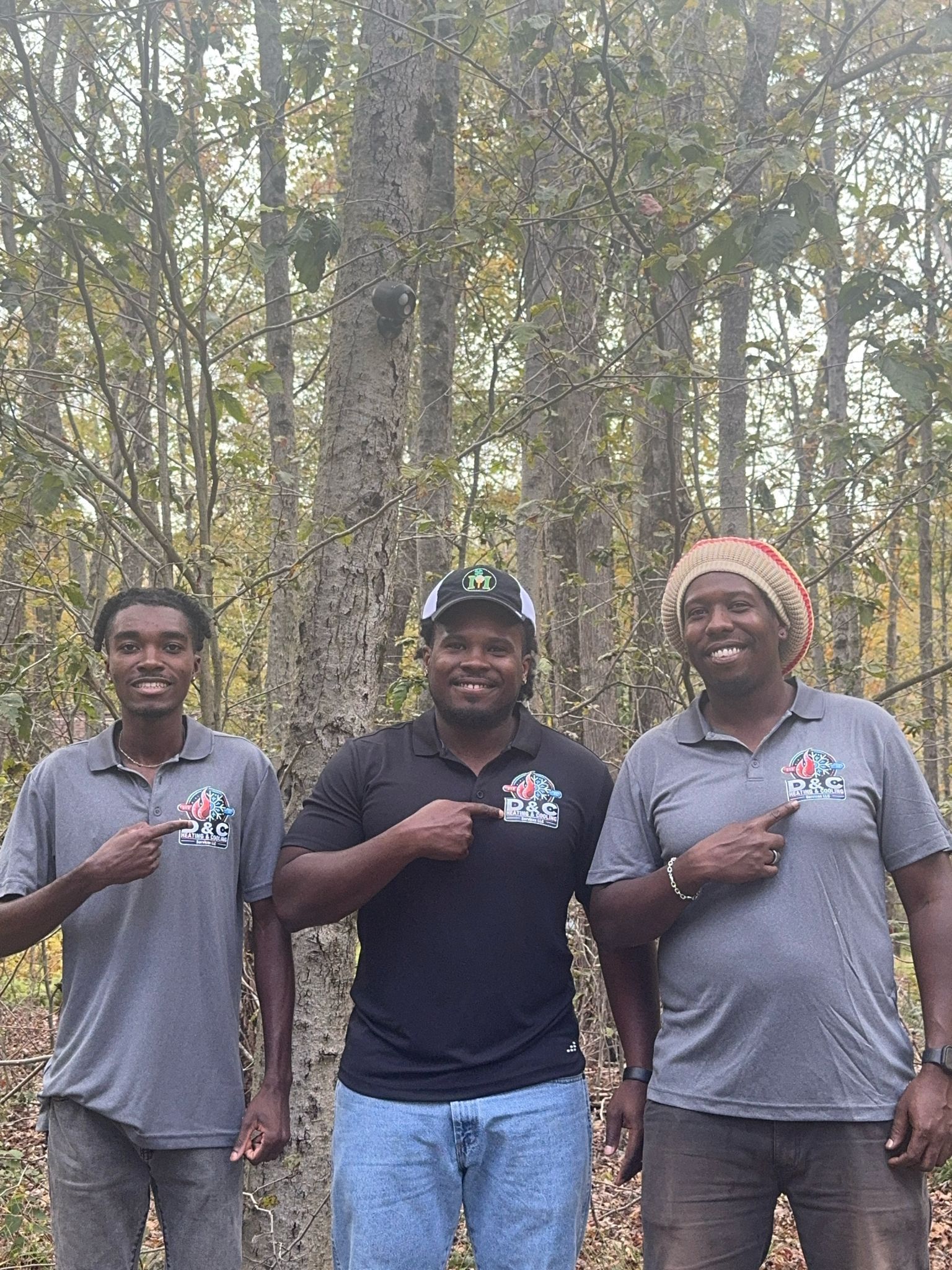 Three people in front of trees, all pointing at a logo on their shirts.