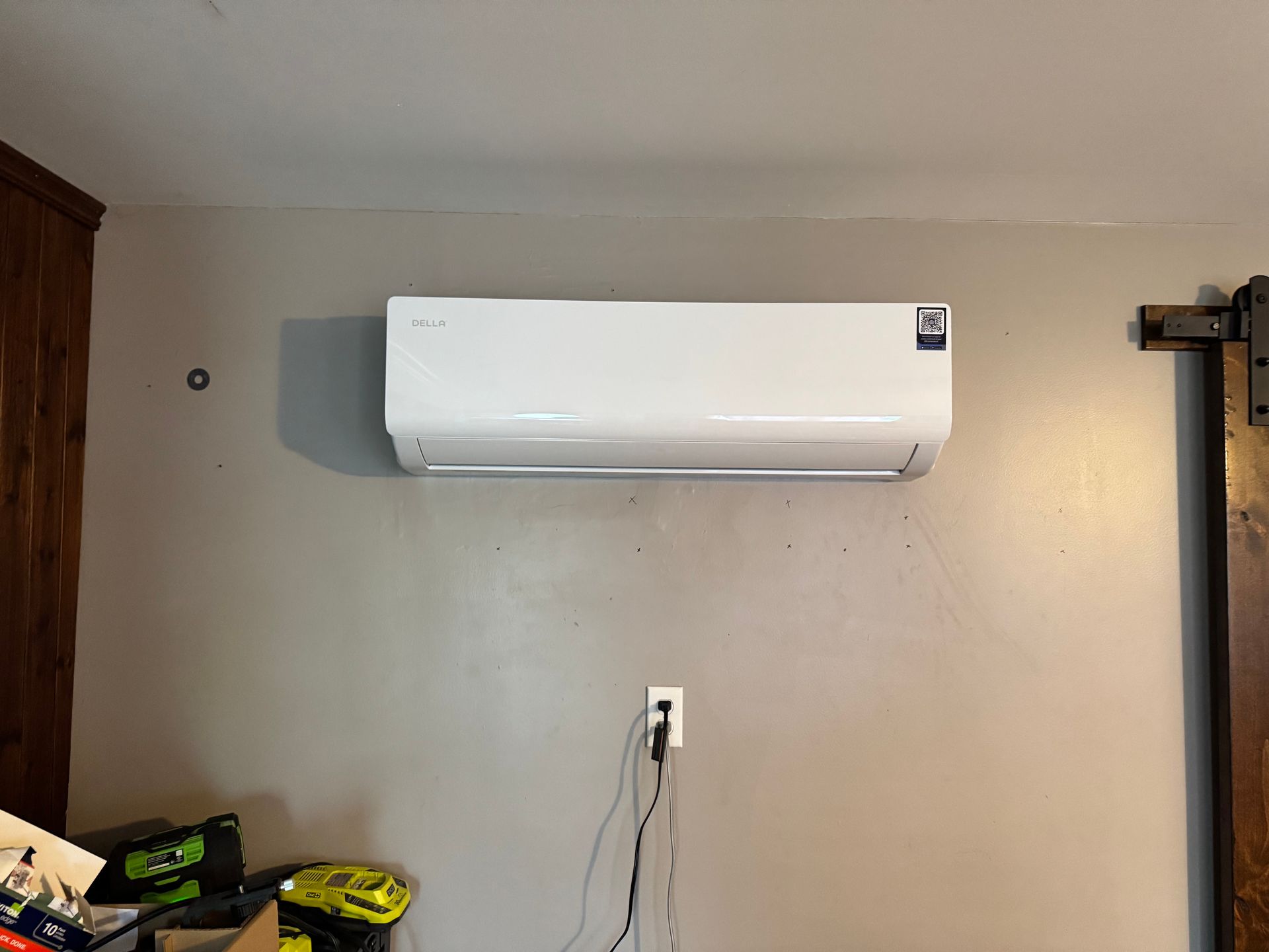 A white wall-mounted air conditioning unit on a gray wall; power outlet below.