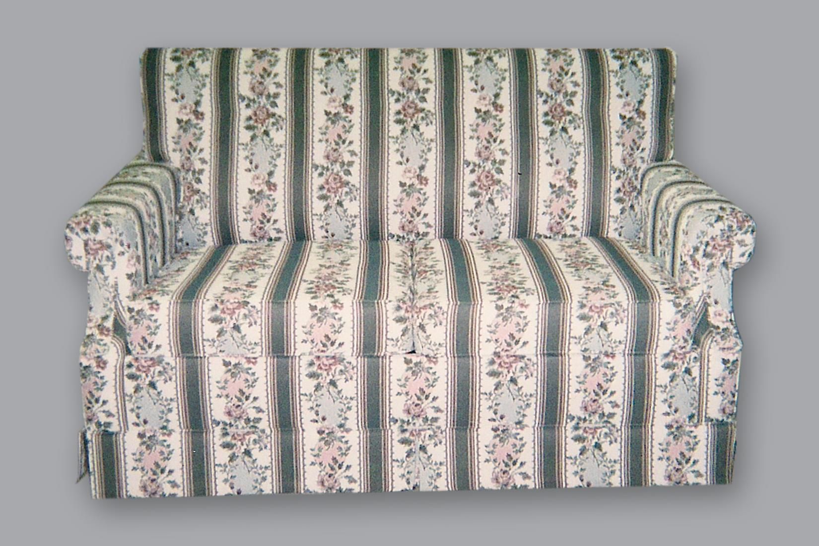 A floral-patterned, two-seater loveseat with vertical stripes and a skirted base, set against a plain gray background.