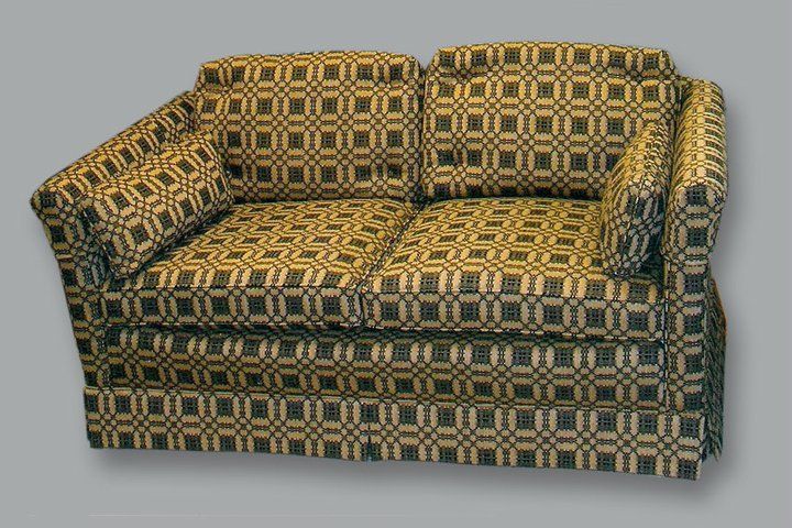 A two-seater loveseat featuring an intricate, repeating geometric pattern in shades of dark green and tan.