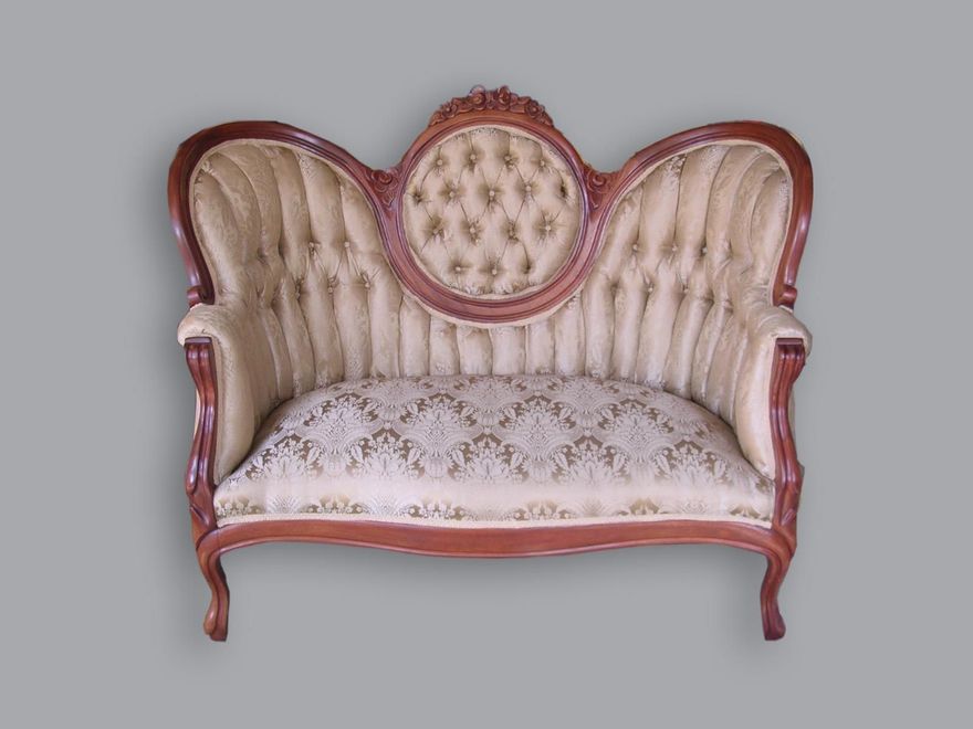 An ornate Victorian-style loveseat with a tufted cream fabric back and a patterned seat cushion, framed in dark wood.
