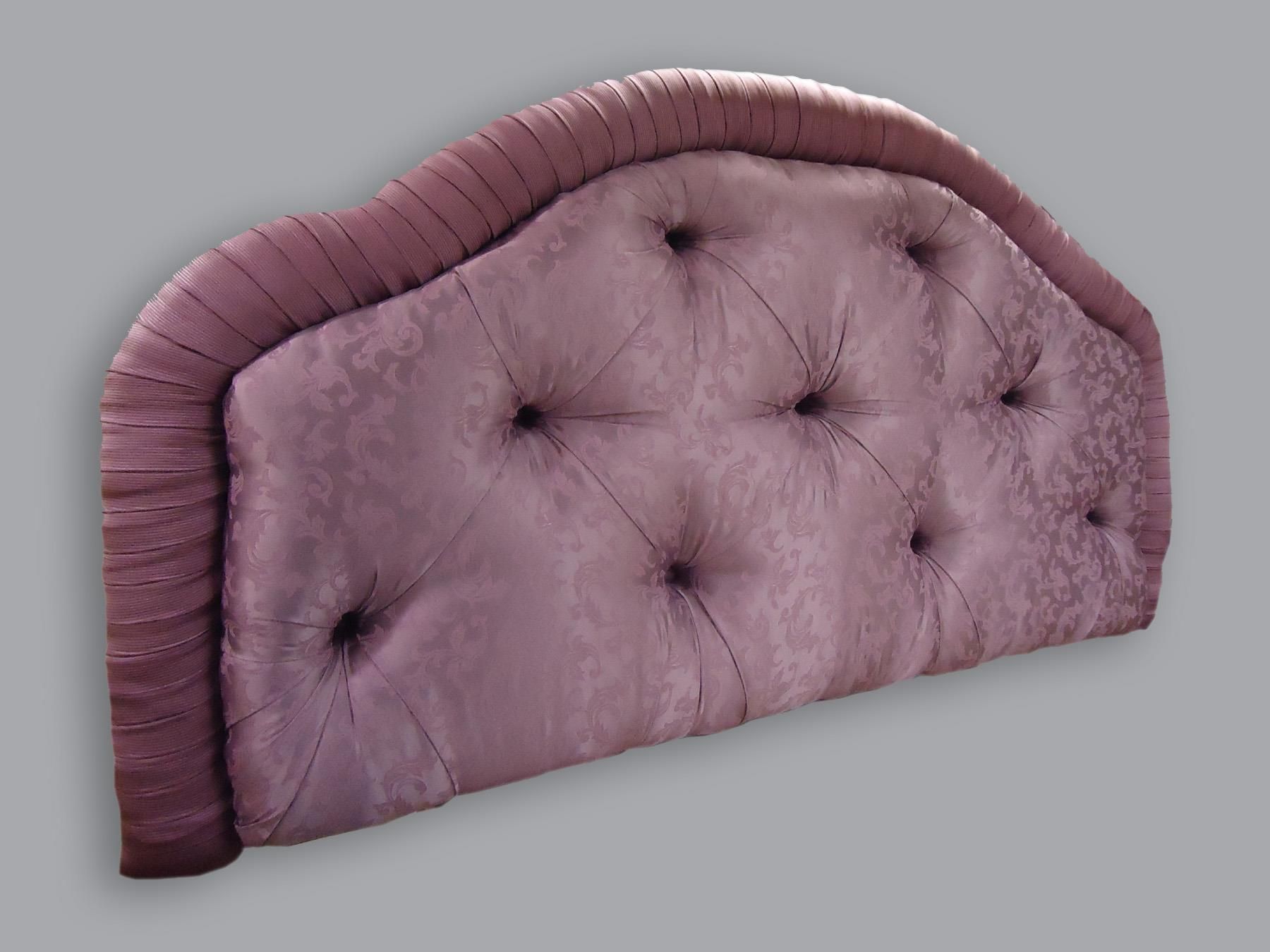 A dusty rose, arched headboard featuring tufted fabric with a decorative, pleated trim border against a gray background.