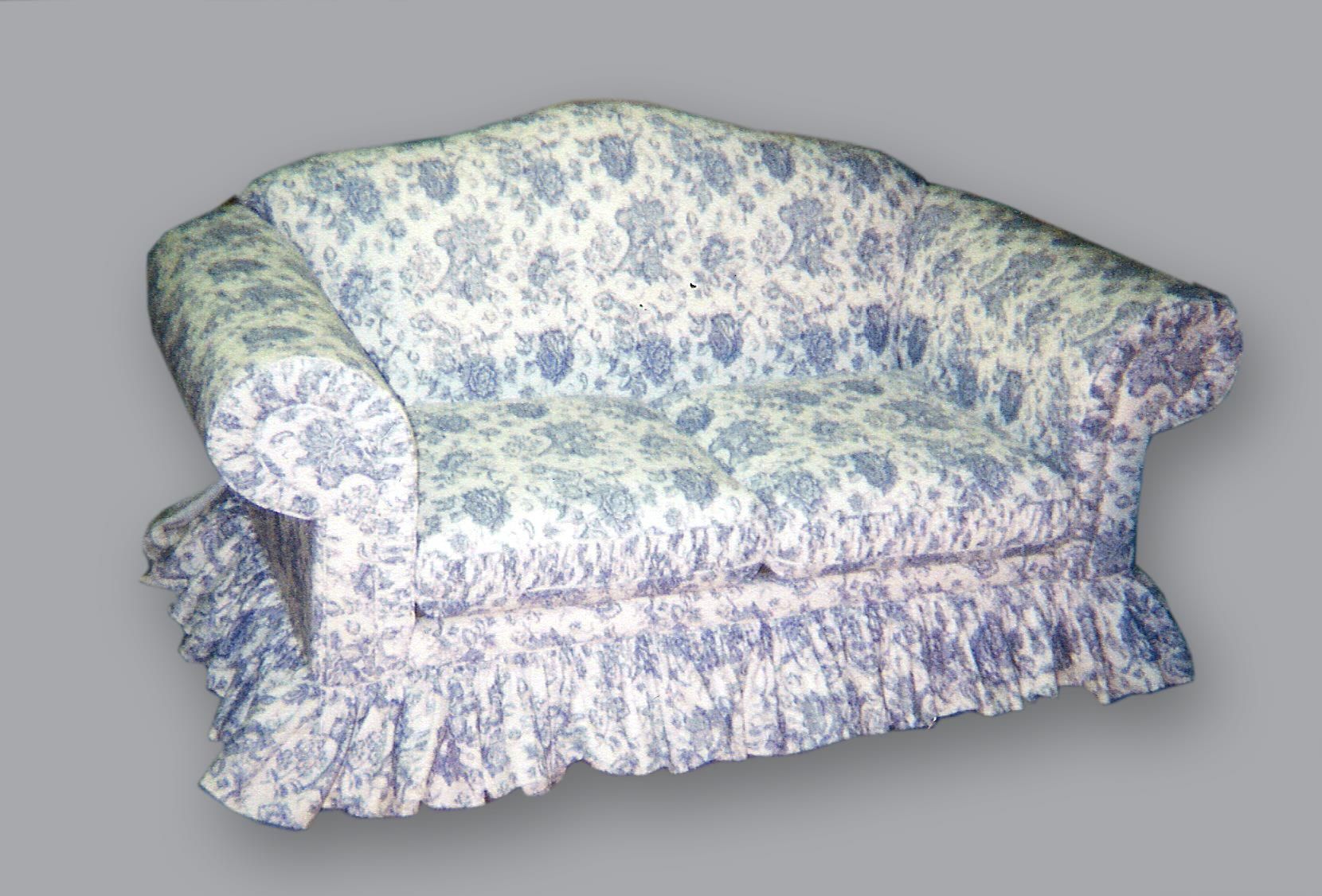 A blue and white floral patterned loveseat with rolled arms and a ruffled skirt, isolated on a light gray background.