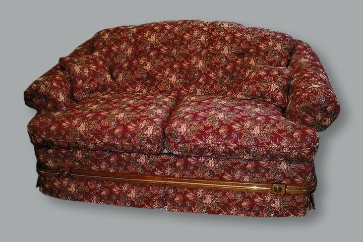 A two-cushion loveseat upholstered in a dark red fabric with a floral pattern, featuring a wooden band along the base.