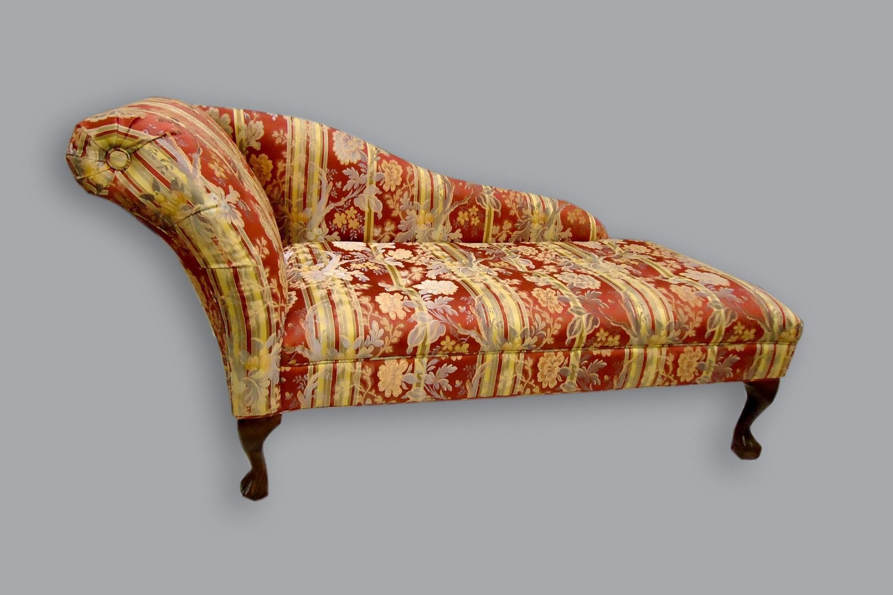 A Victorian-style chaise lounge with red and gold floral patterned upholstery, set on dark wood cabriole legs.