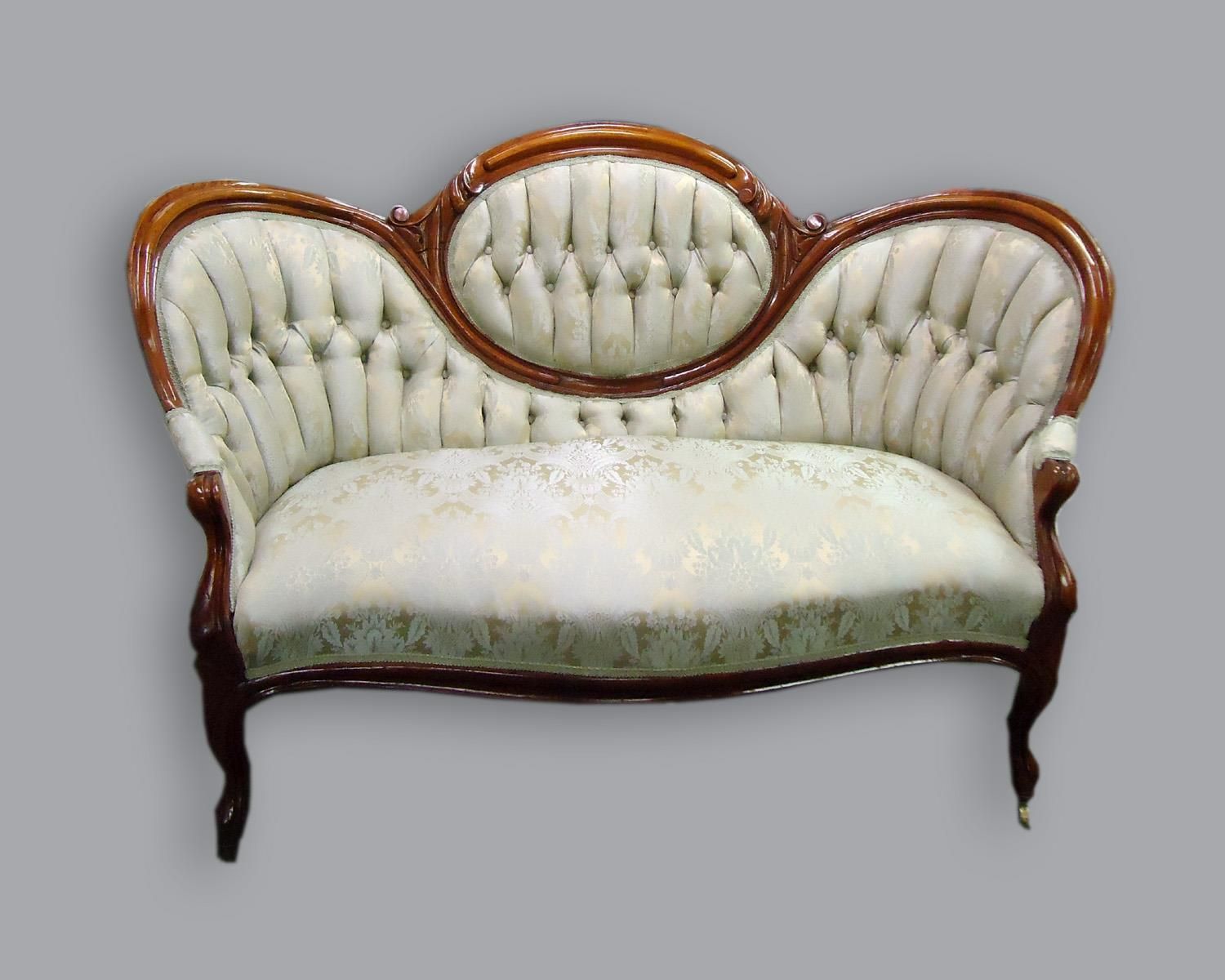 Victorian-style loveseat with a dark wood frame, tufted cream upholstery, and a prominent oval backrest cushion.