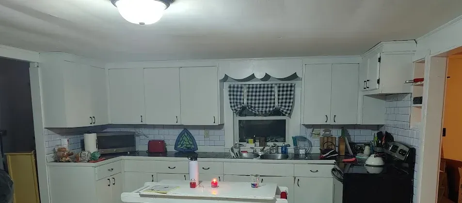 A kitchen with white cabinets, a black stove, and a window with a checkered curtain.
