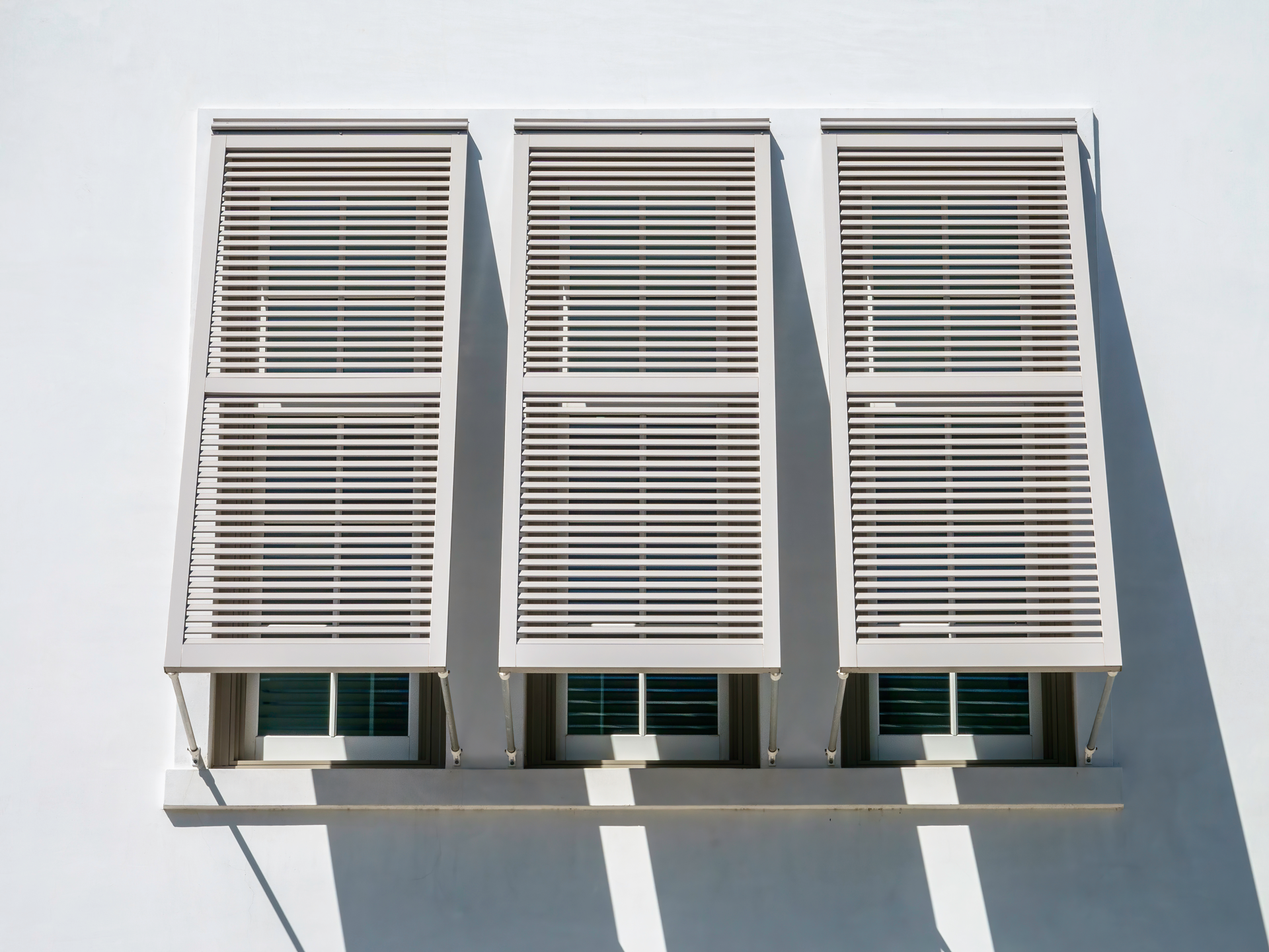 Three windows on a white building with shutters on them