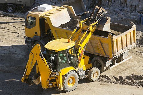 una scavatrice di color giallo sta caricando della terra nel rimorchio di un camion da lavoro