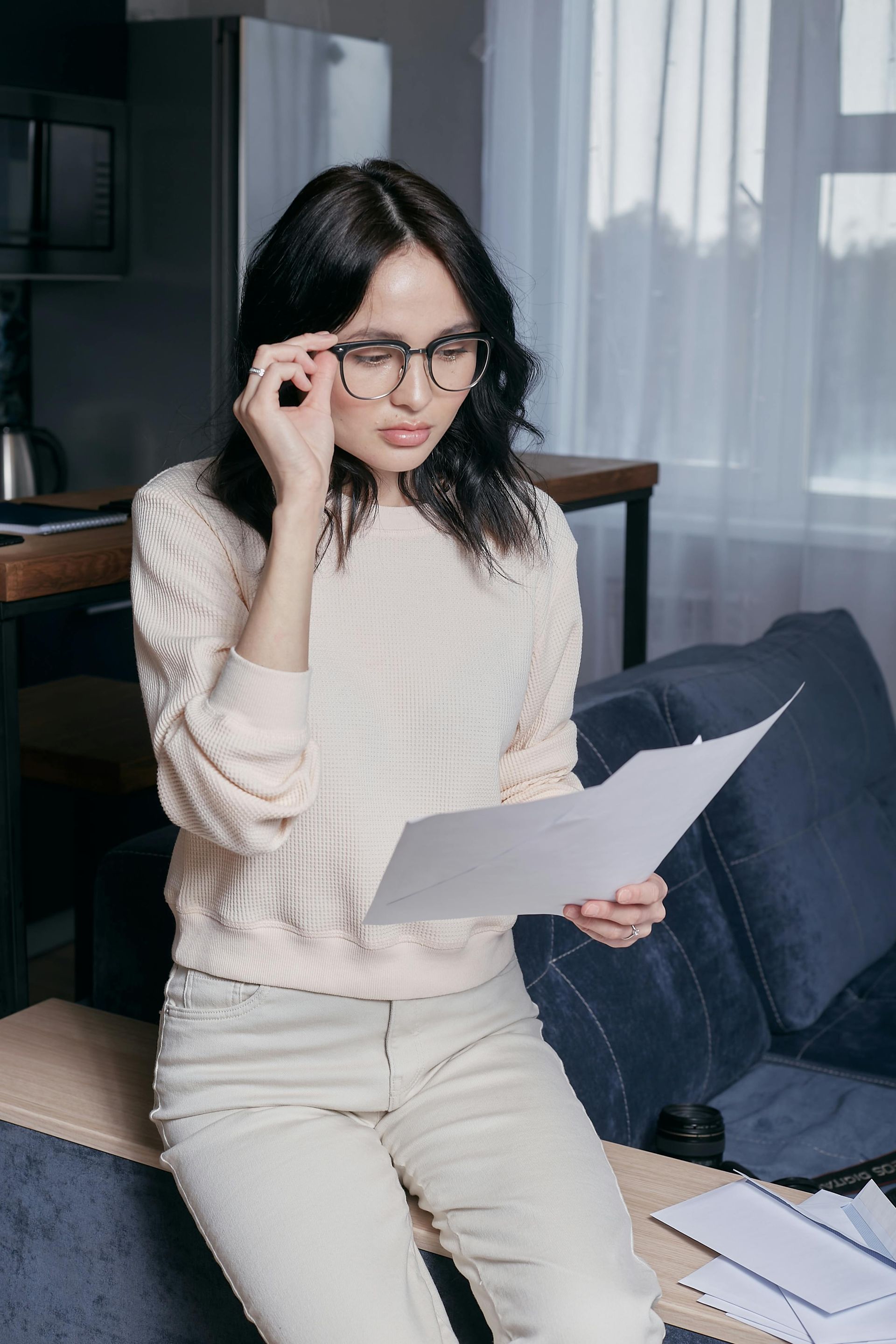 A woman wearing glasses is sitting on a couch reading a piece of paper.