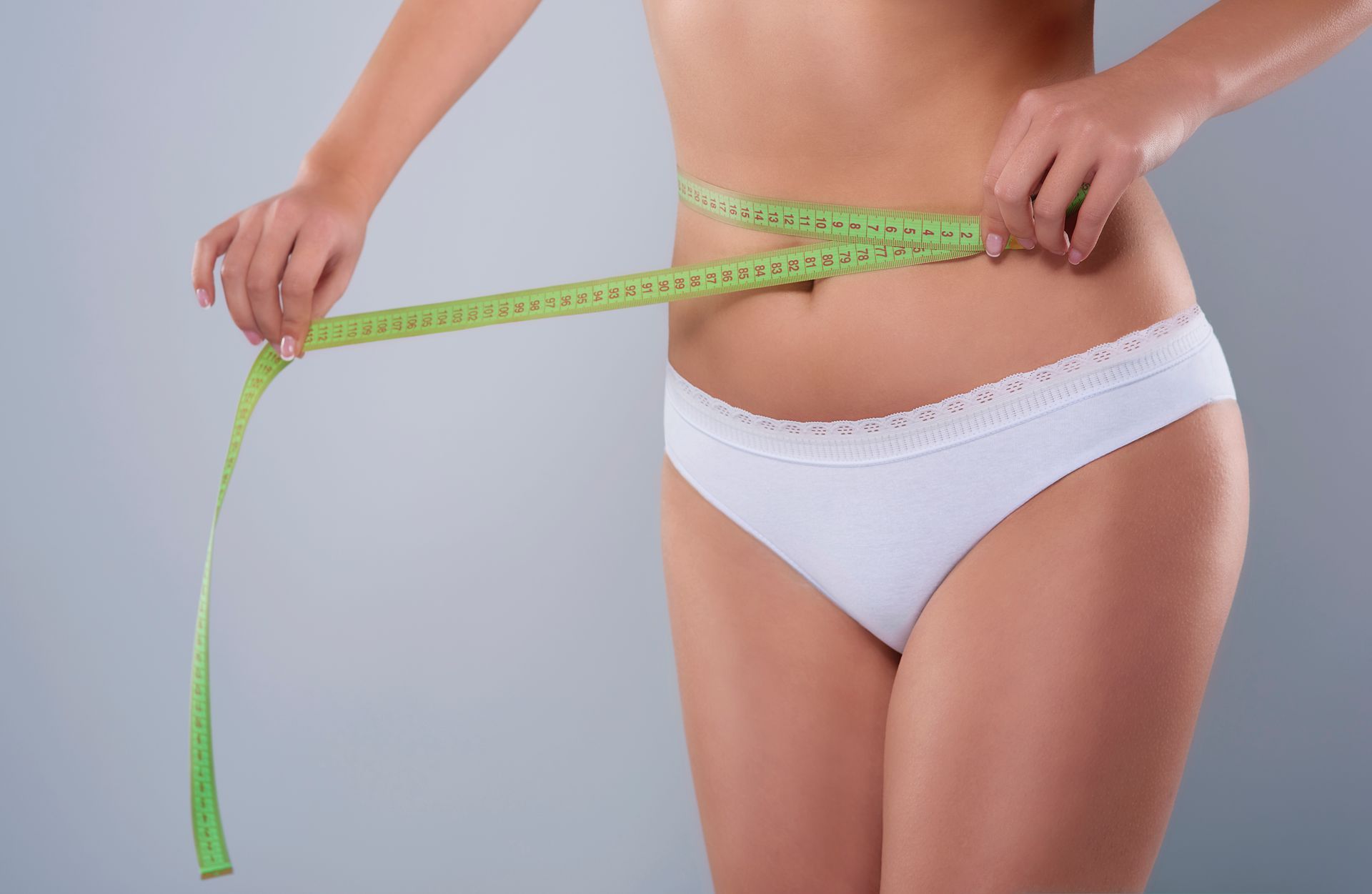 Una mujer en ropa interior blanca mide su cintura con una cinta métrica.