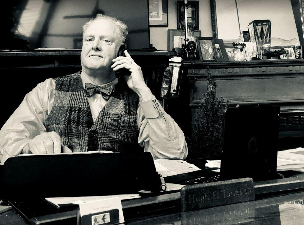 A man is sitting at a desk talking on a cell phone