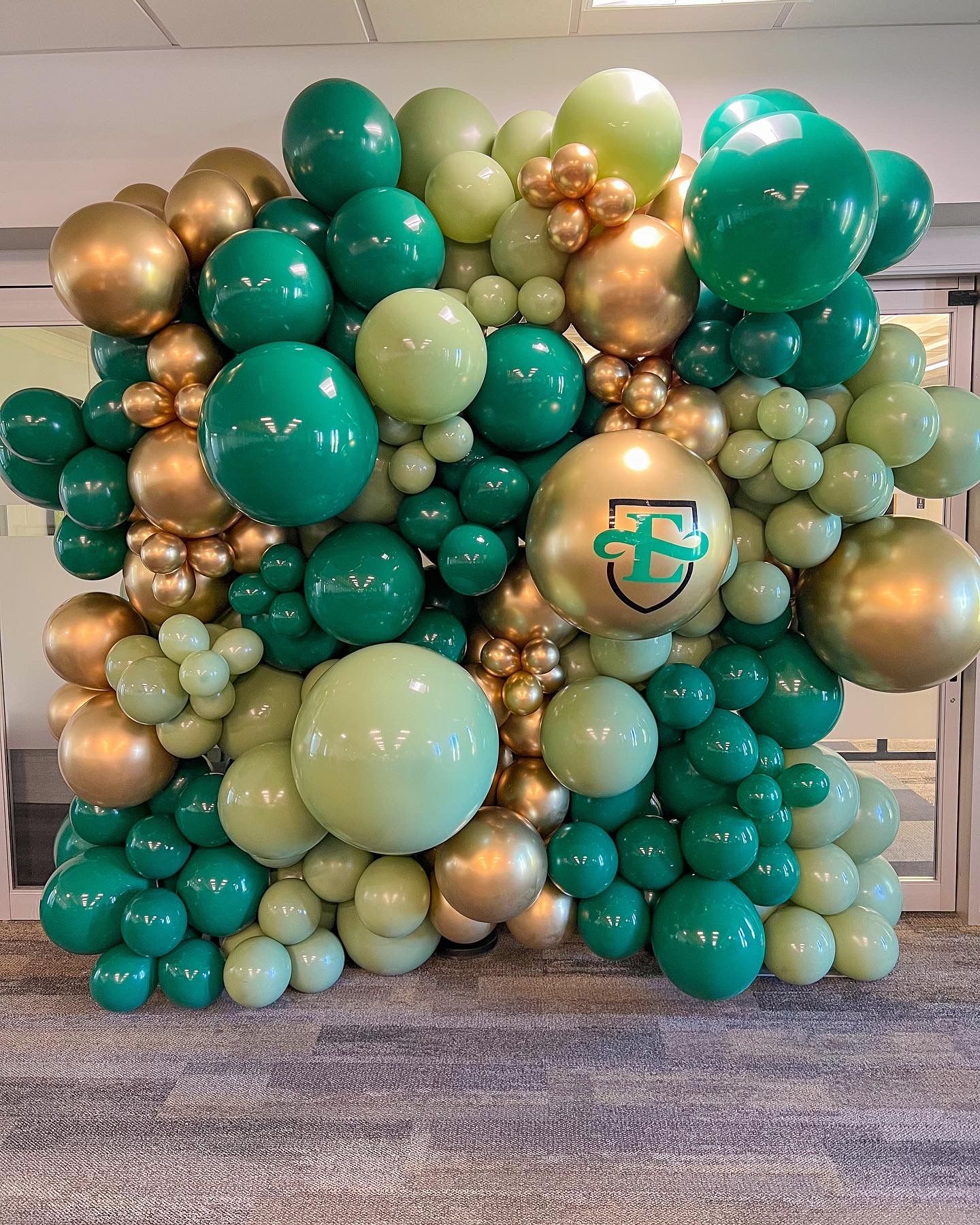 A wall of green and gold balloons in a room.