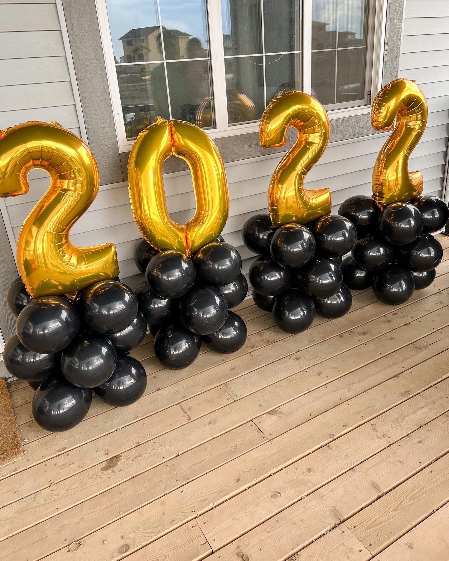 A bunch of black and gold balloons are sitting on a wooden deck.