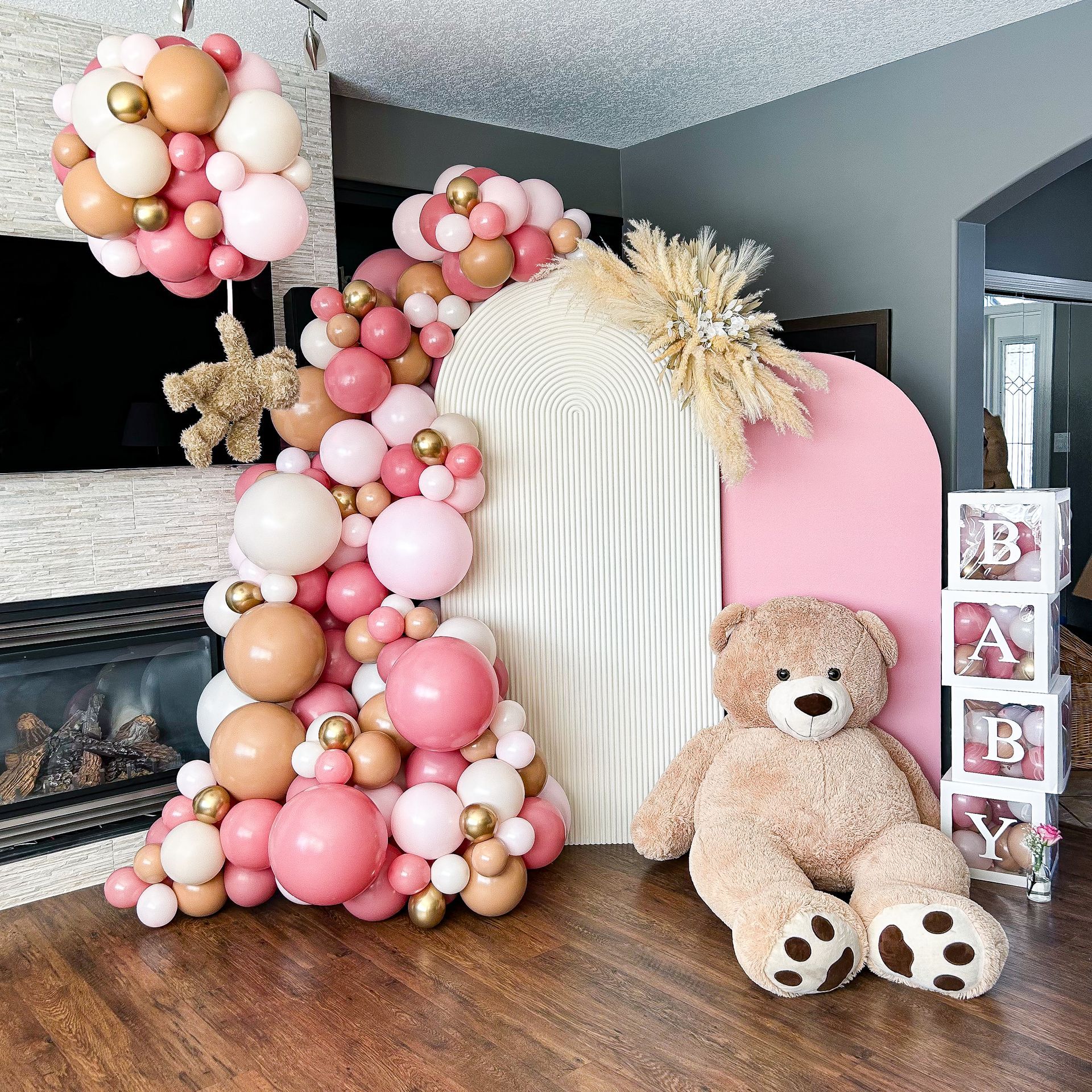 A teddy bear is sitting in front of a wall made of balloons.