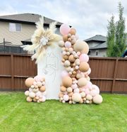 A bunch of balloons are sitting on the grass in front of a wooden fence.