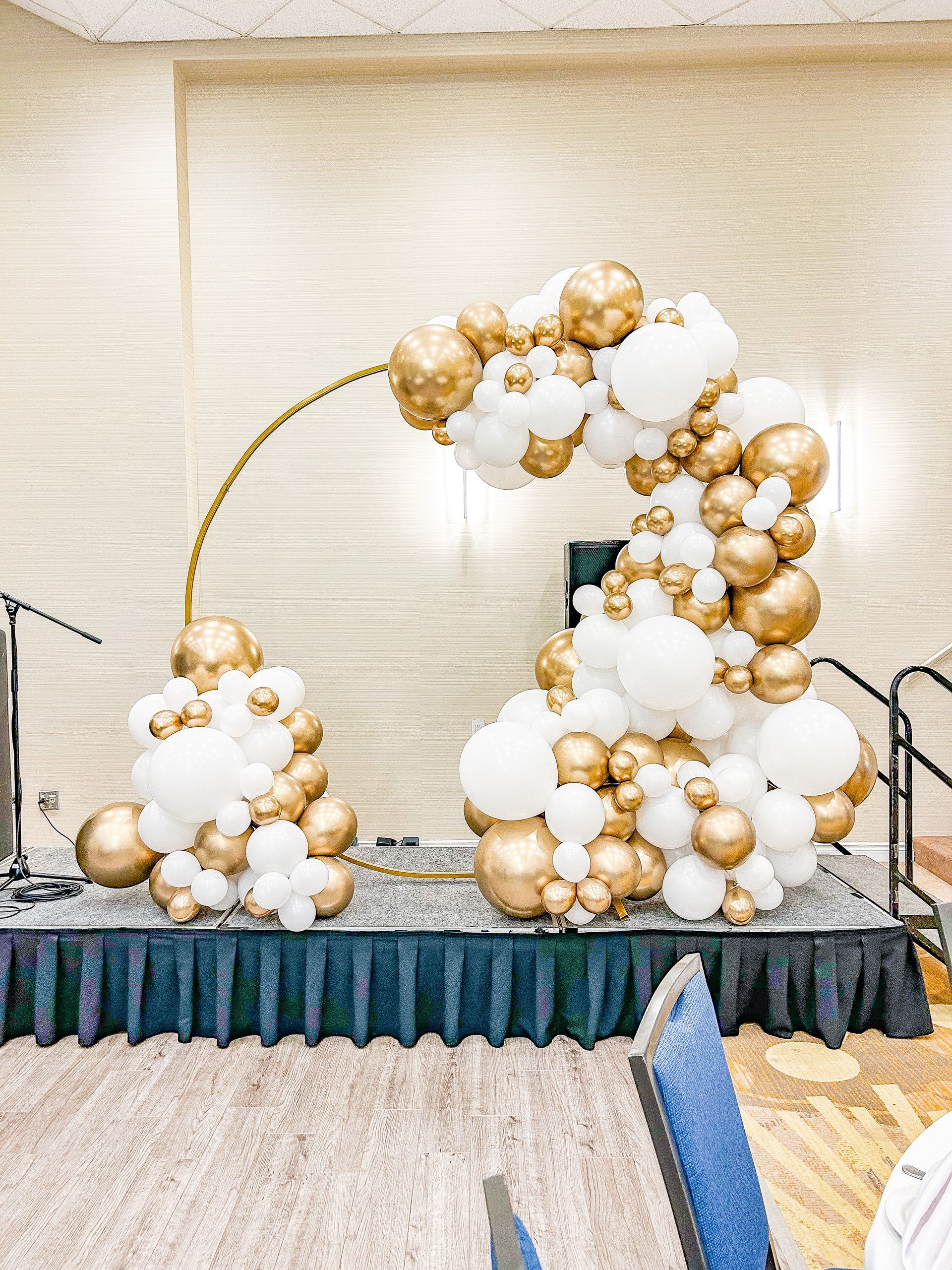 A stage decorated with white and gold balloons in a room.