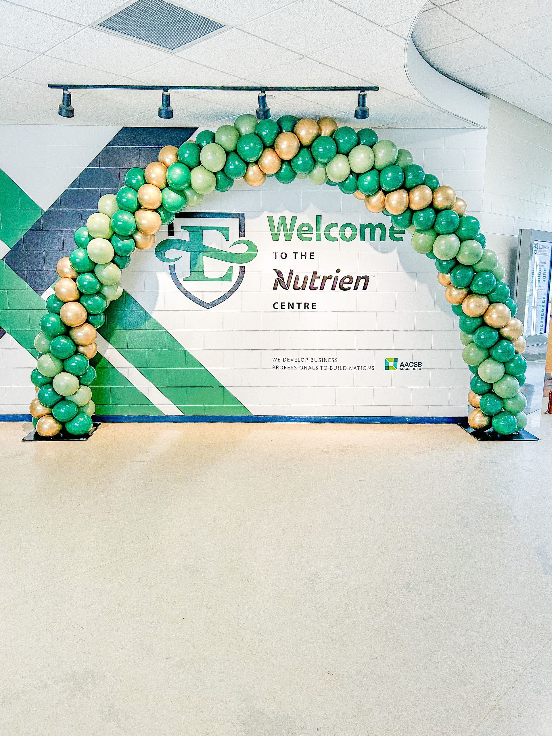 A green and gold balloon arch in front of a welcome sign