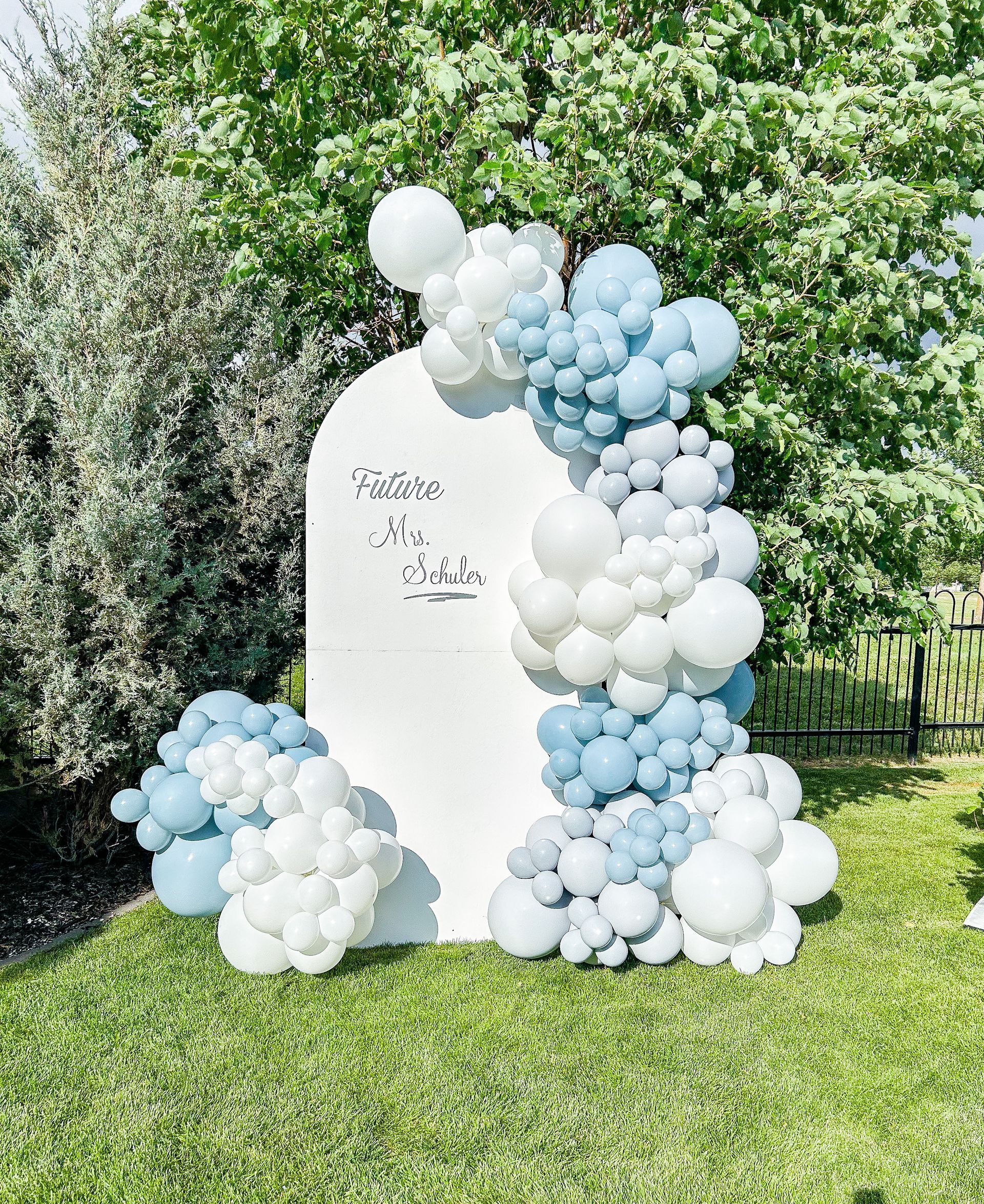 A white arch surrounded by blue and white balloons on a lush green field.
