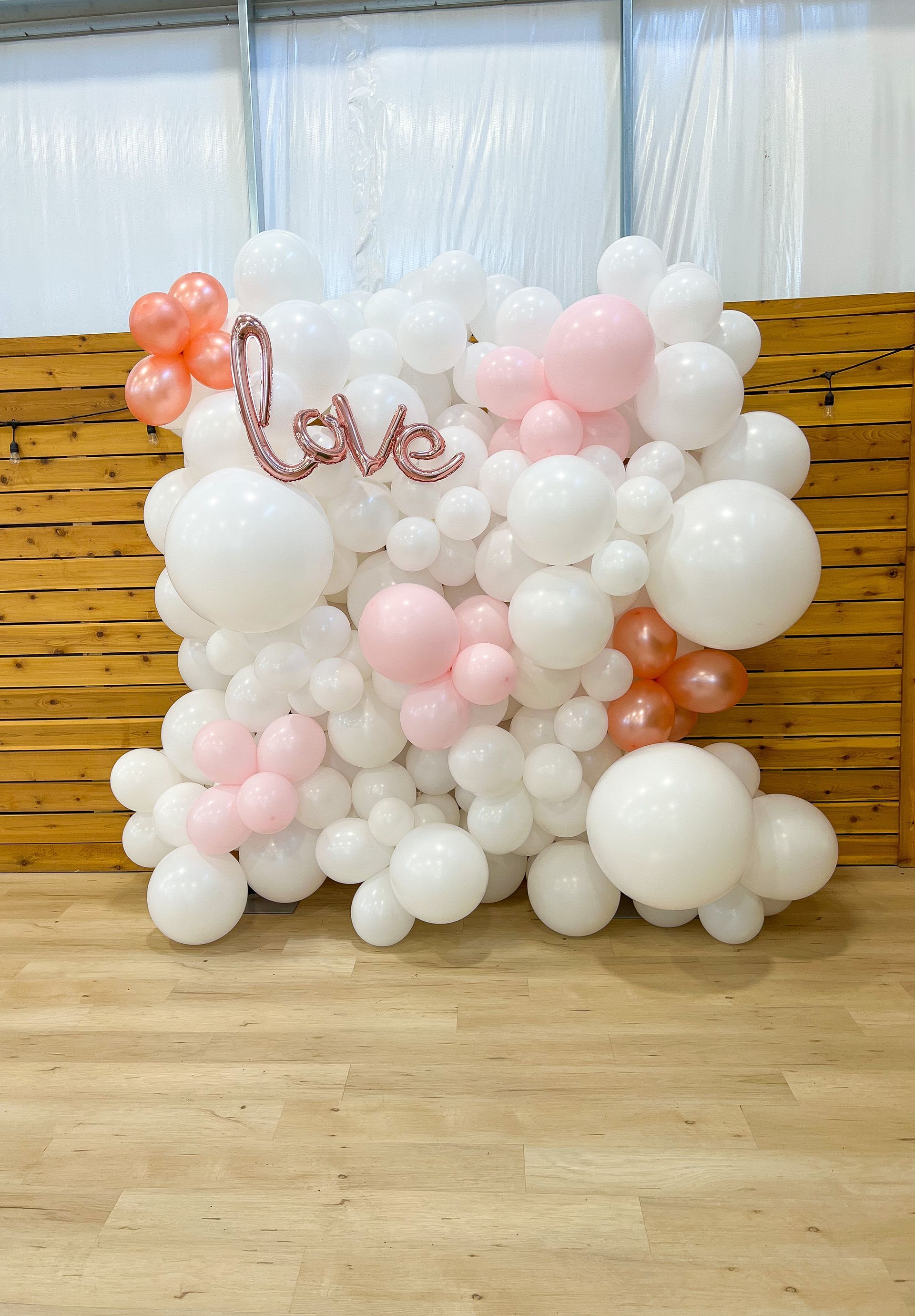 A wall of white and pink balloons with the word love written on it.