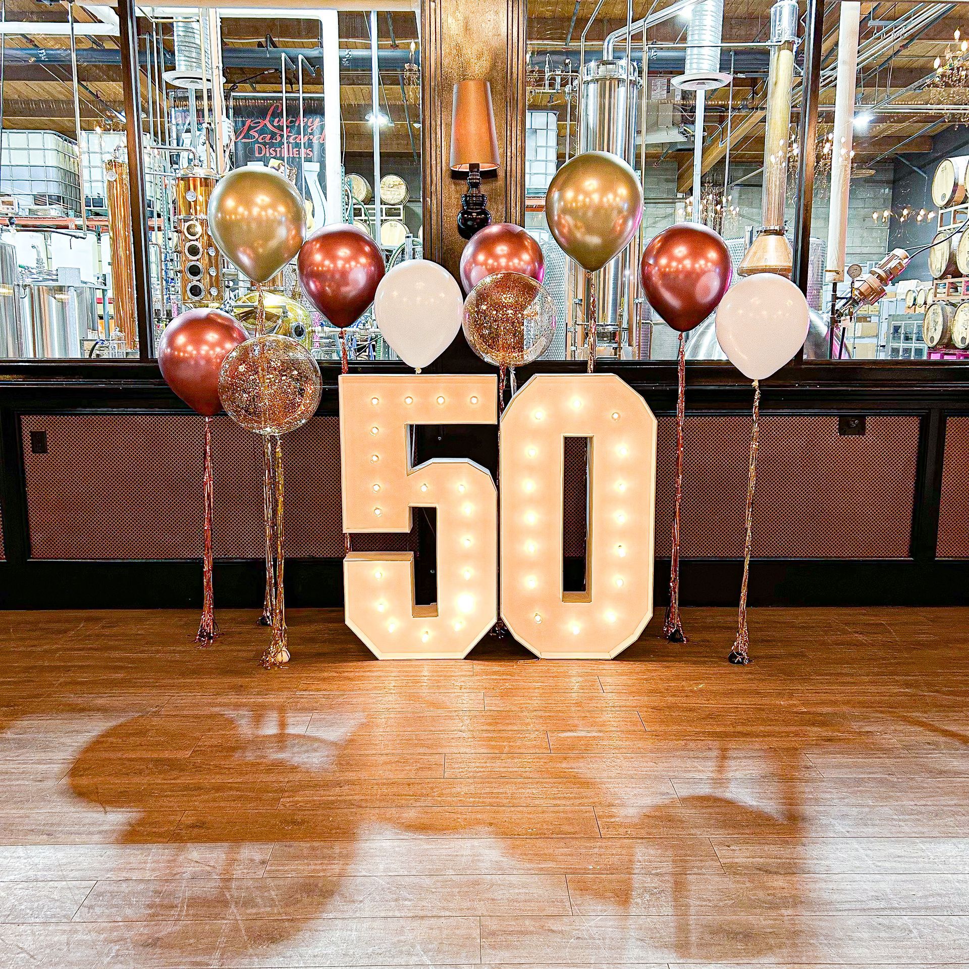 A large number 50 is surrounded by balloons on a wooden floor.