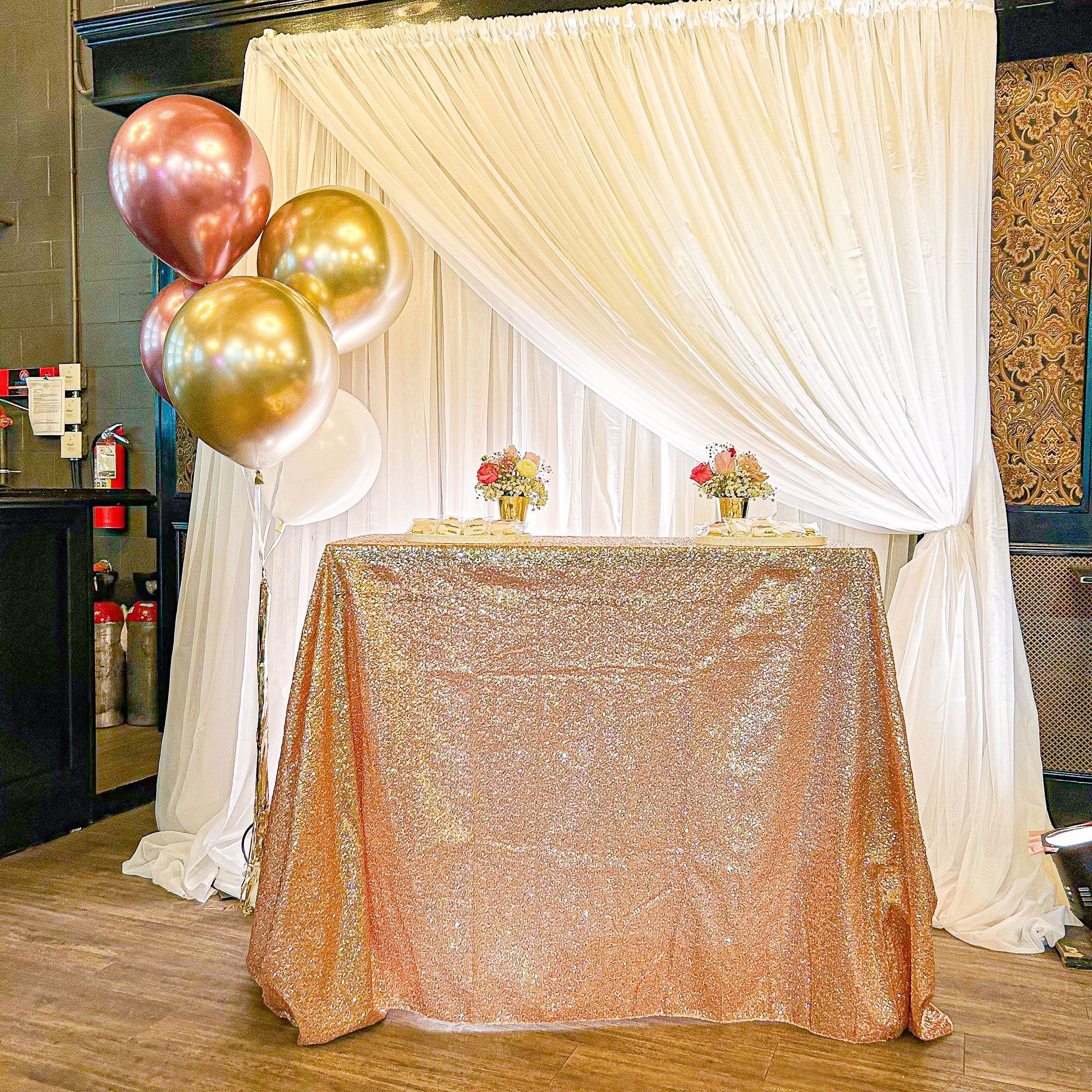 A table with a sequined tablecloth and balloons in front of a white curtain.