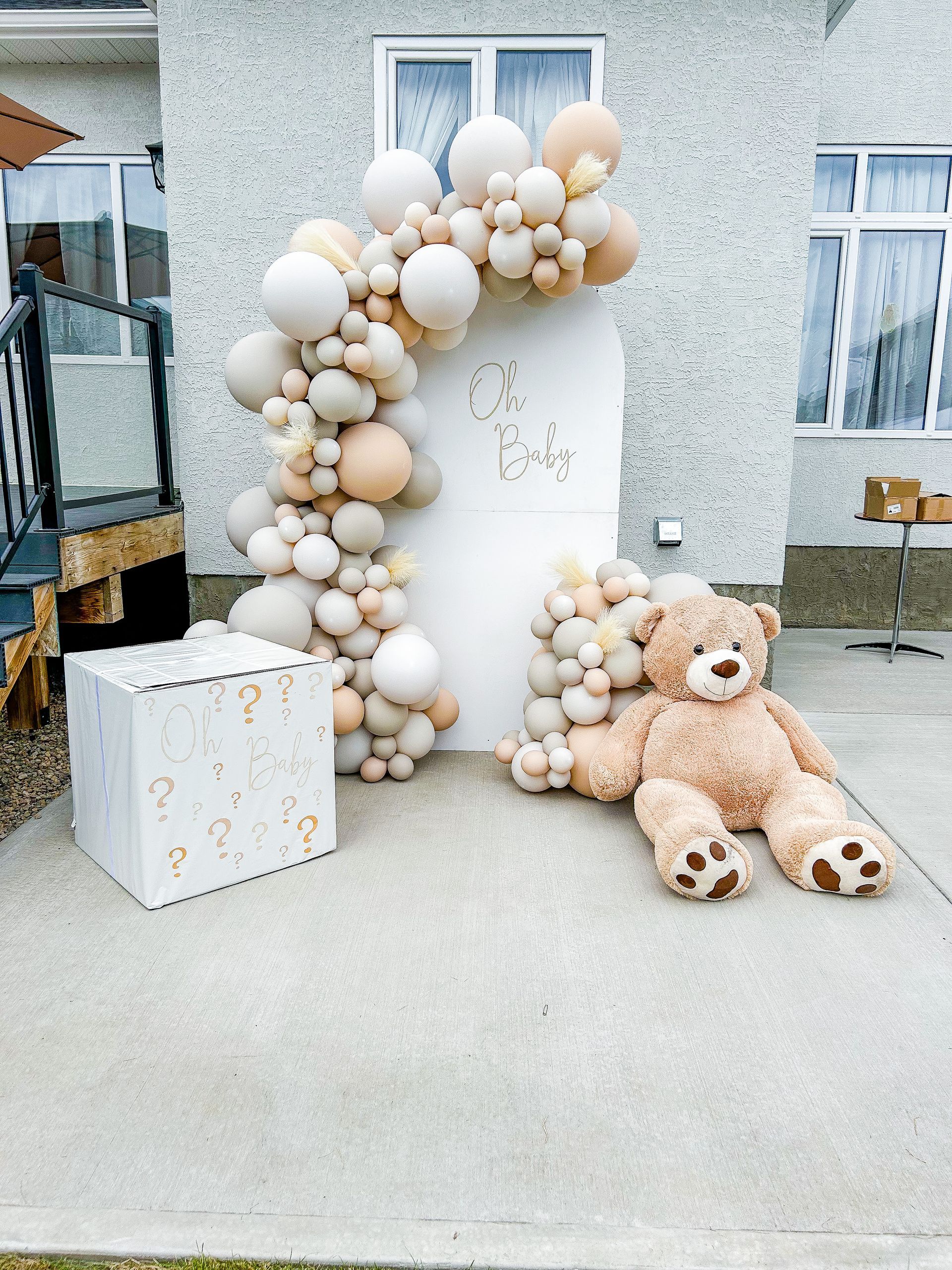 A teddy bear is sitting in front of a balloon arch.