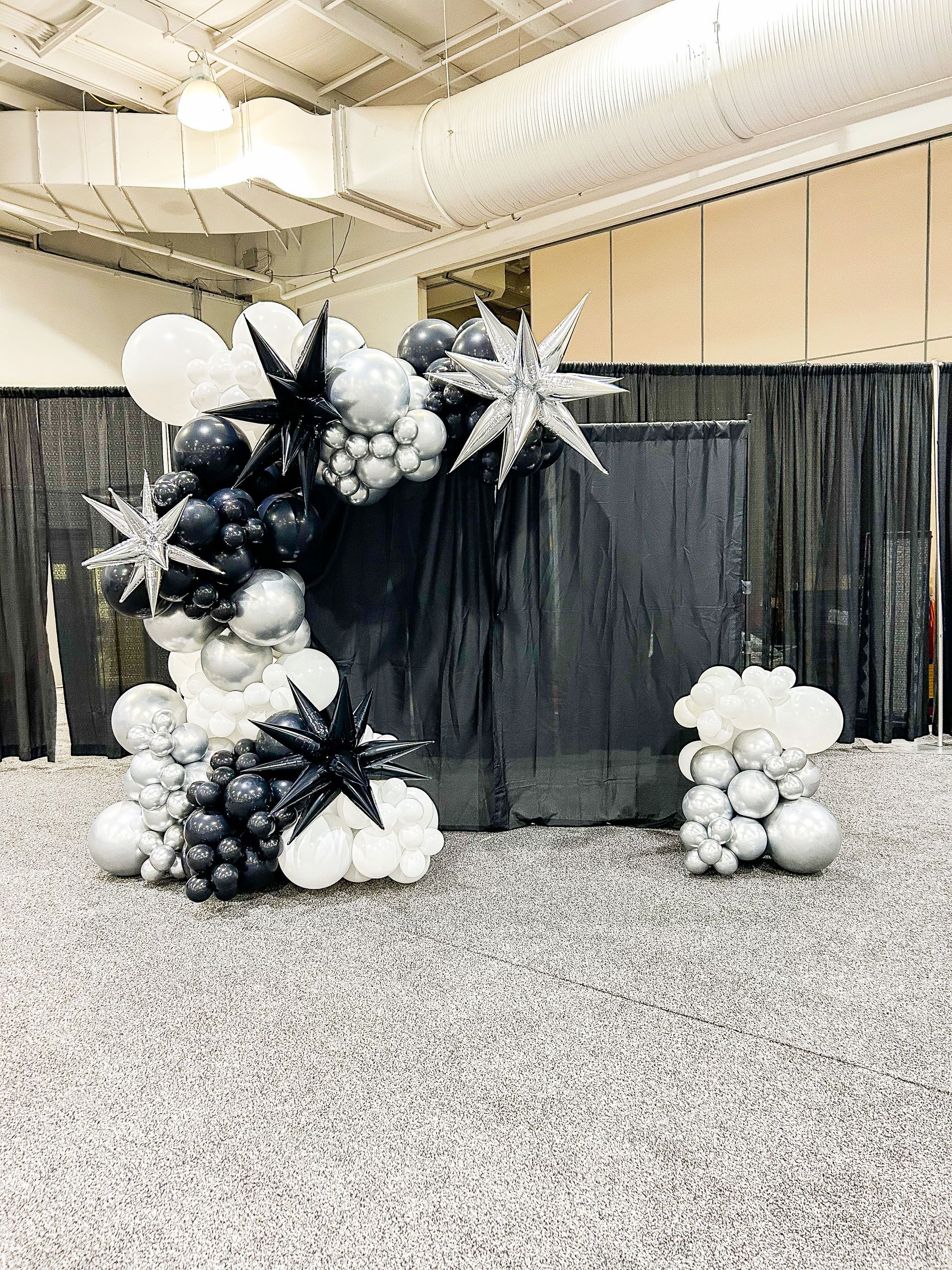 A bunch of balloons are sitting on the floor in front of a black curtain.