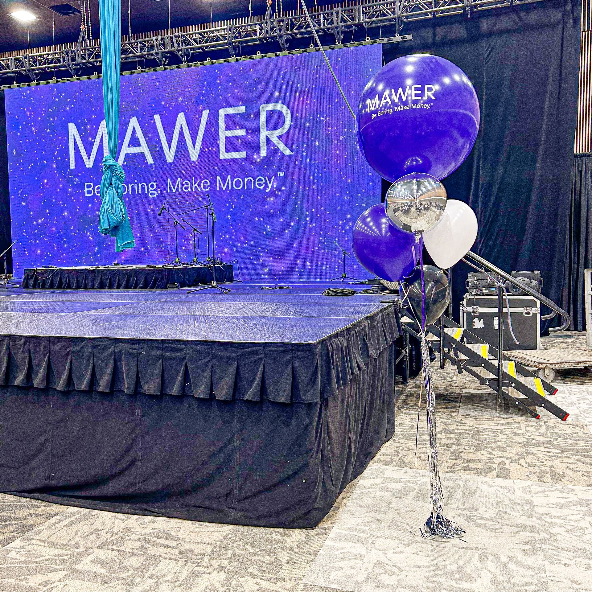 A stage with purple balloons in front of a mawer sign