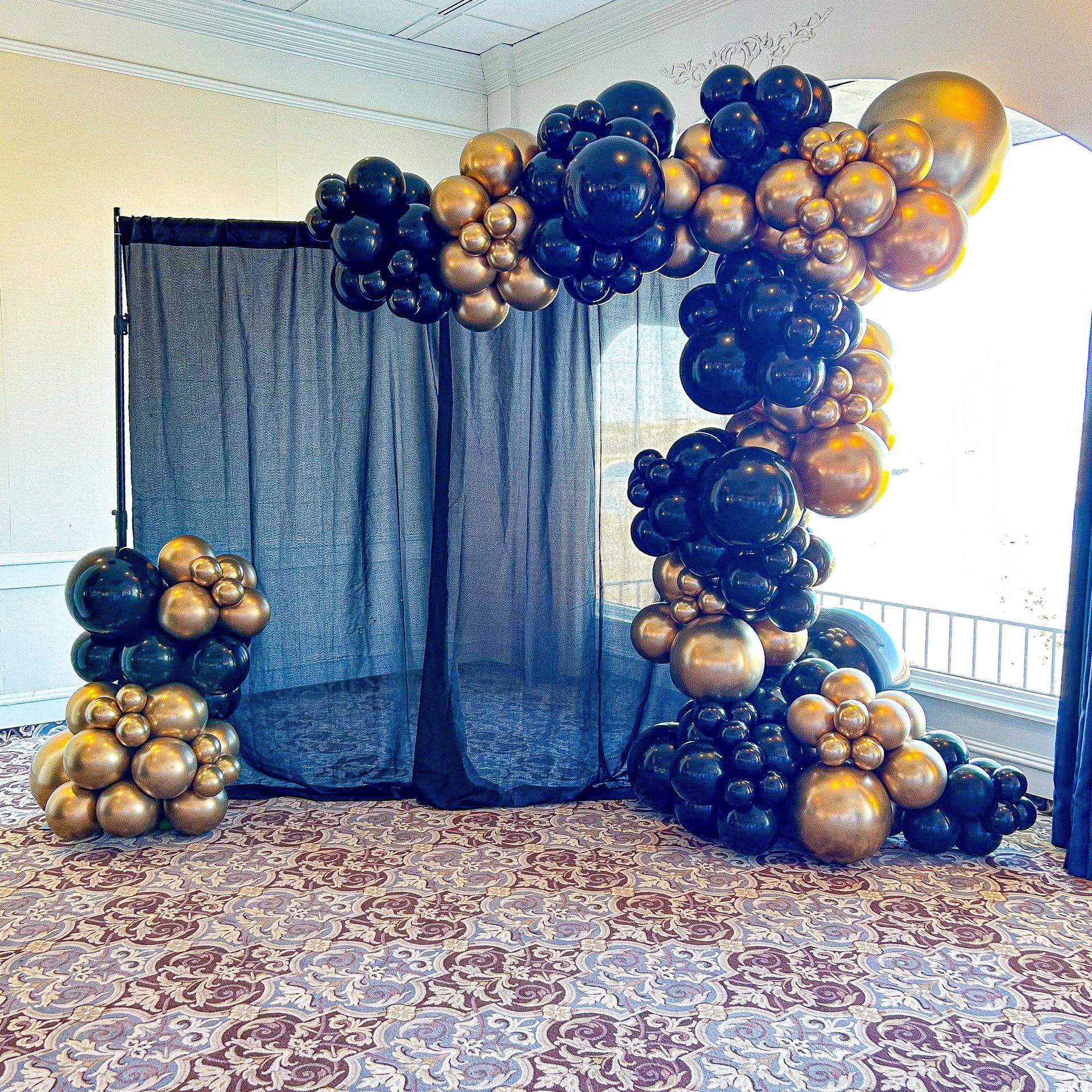 A room decorated with black and gold balloons and a black curtain.