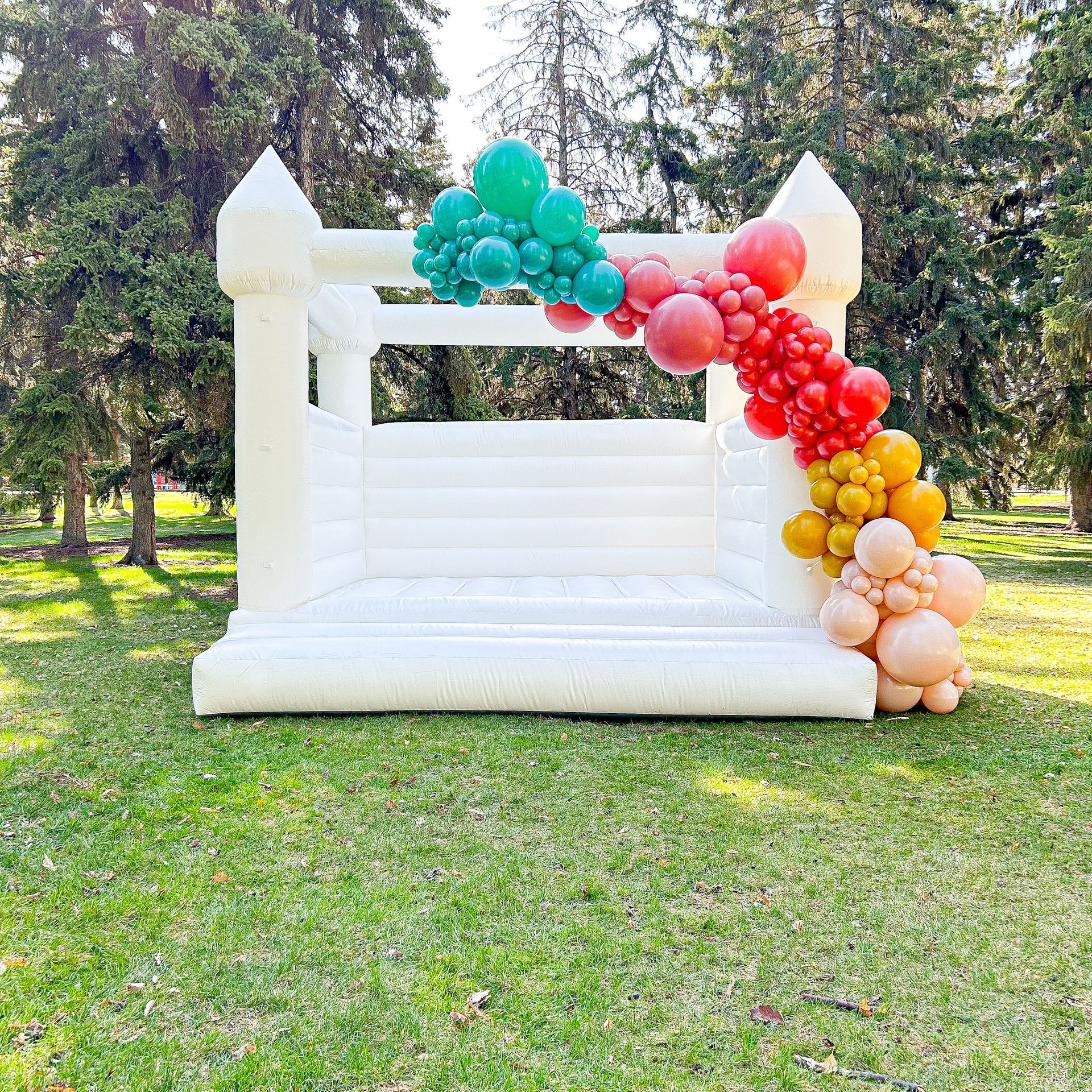A white bouncy castle is decorated with balloons in a park.