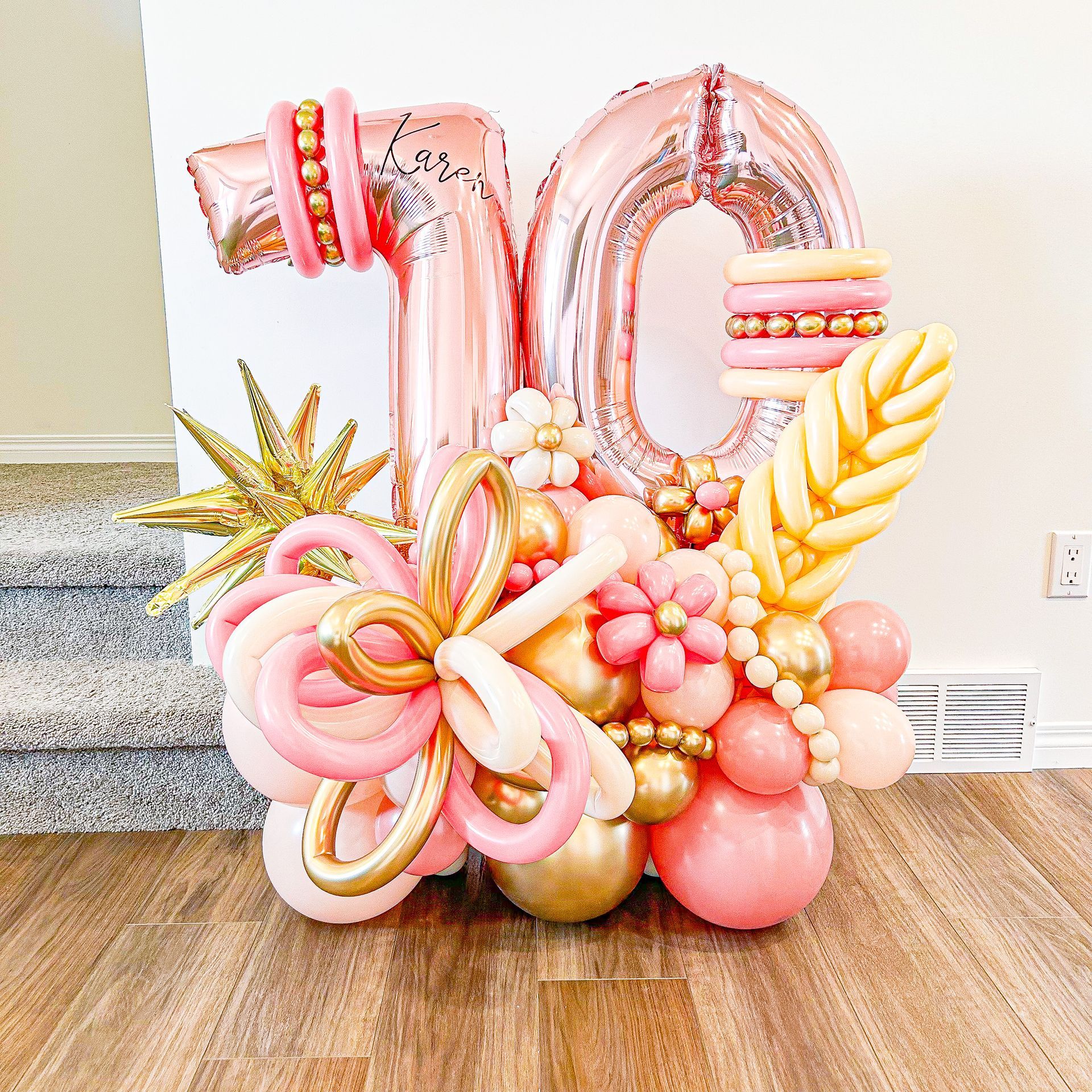 A bunch of pink and gold balloons are sitting on a wooden floor.