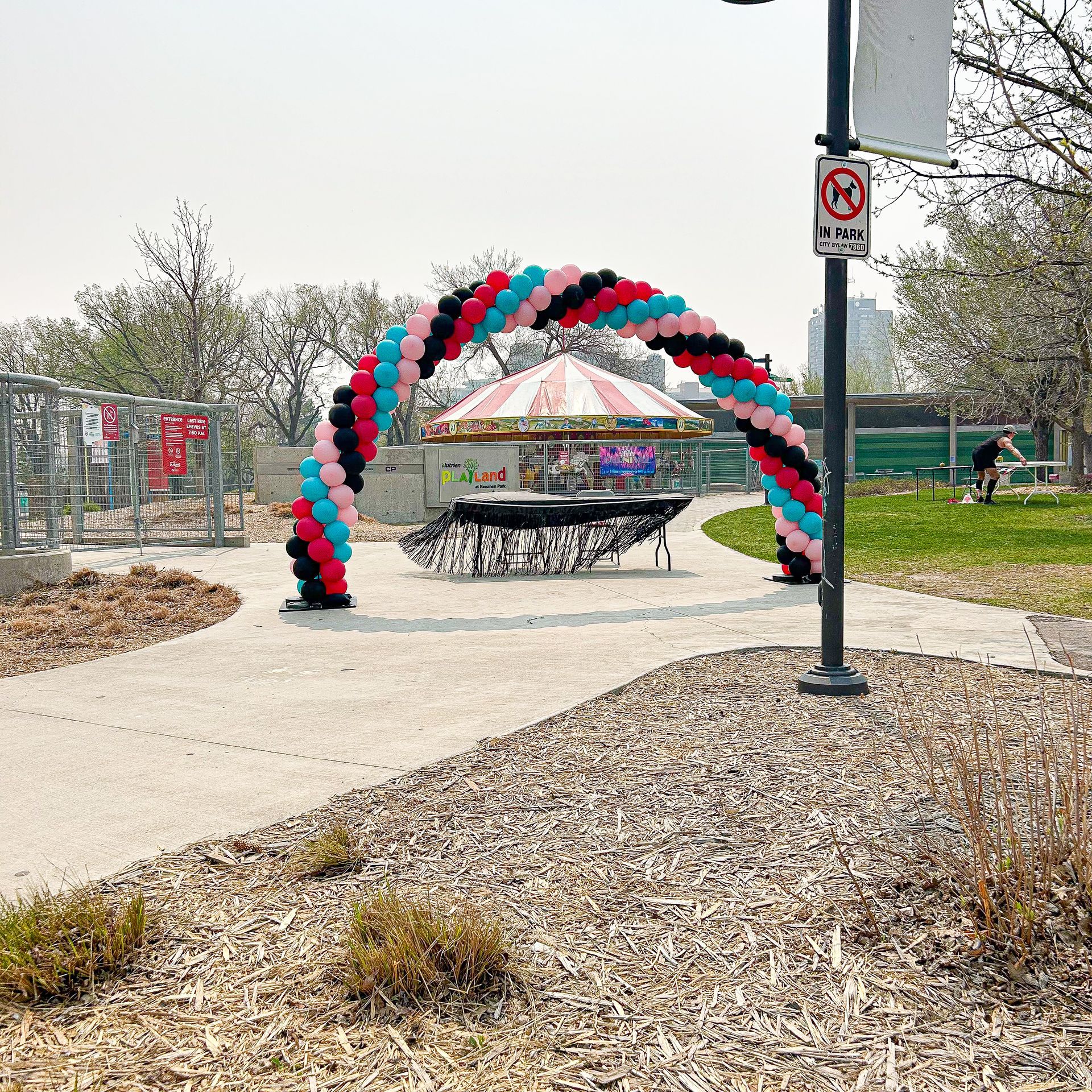A balloon arch in a park with a no parking sign