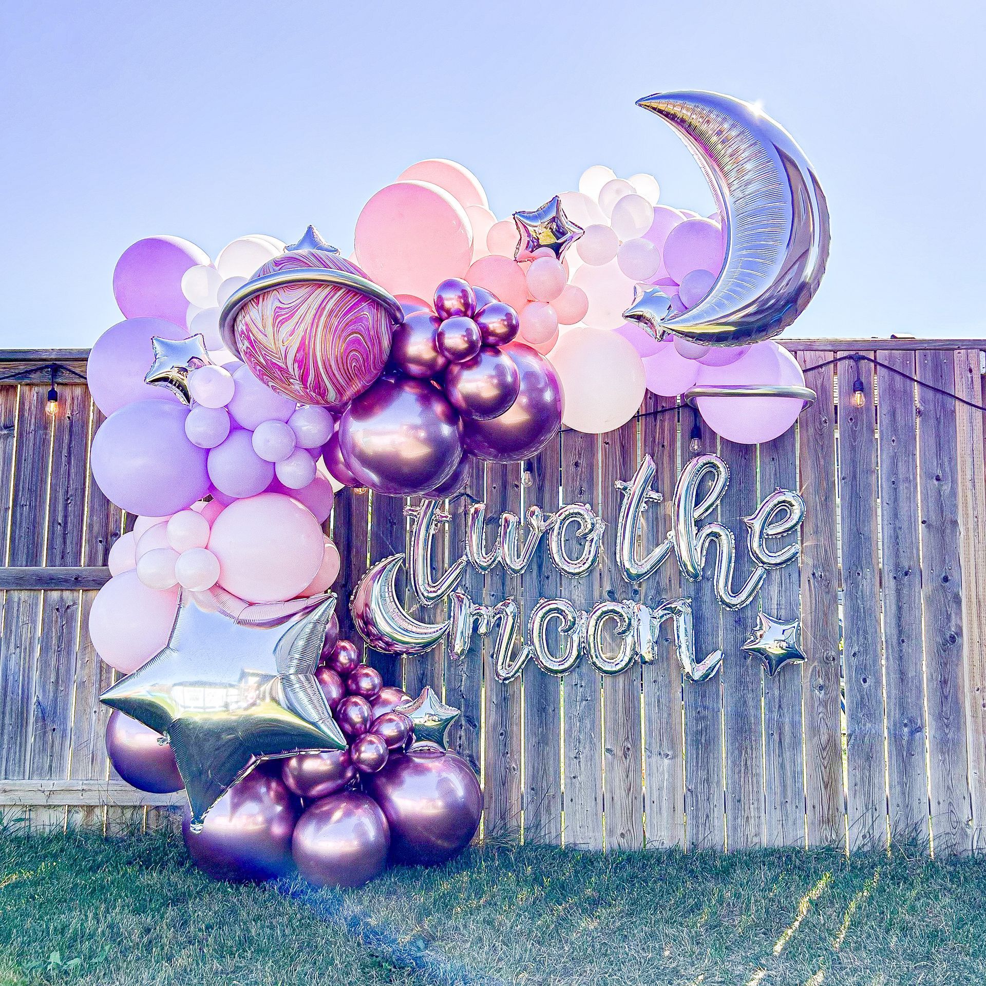 A bunch of balloons are sitting on top of a wooden fence.