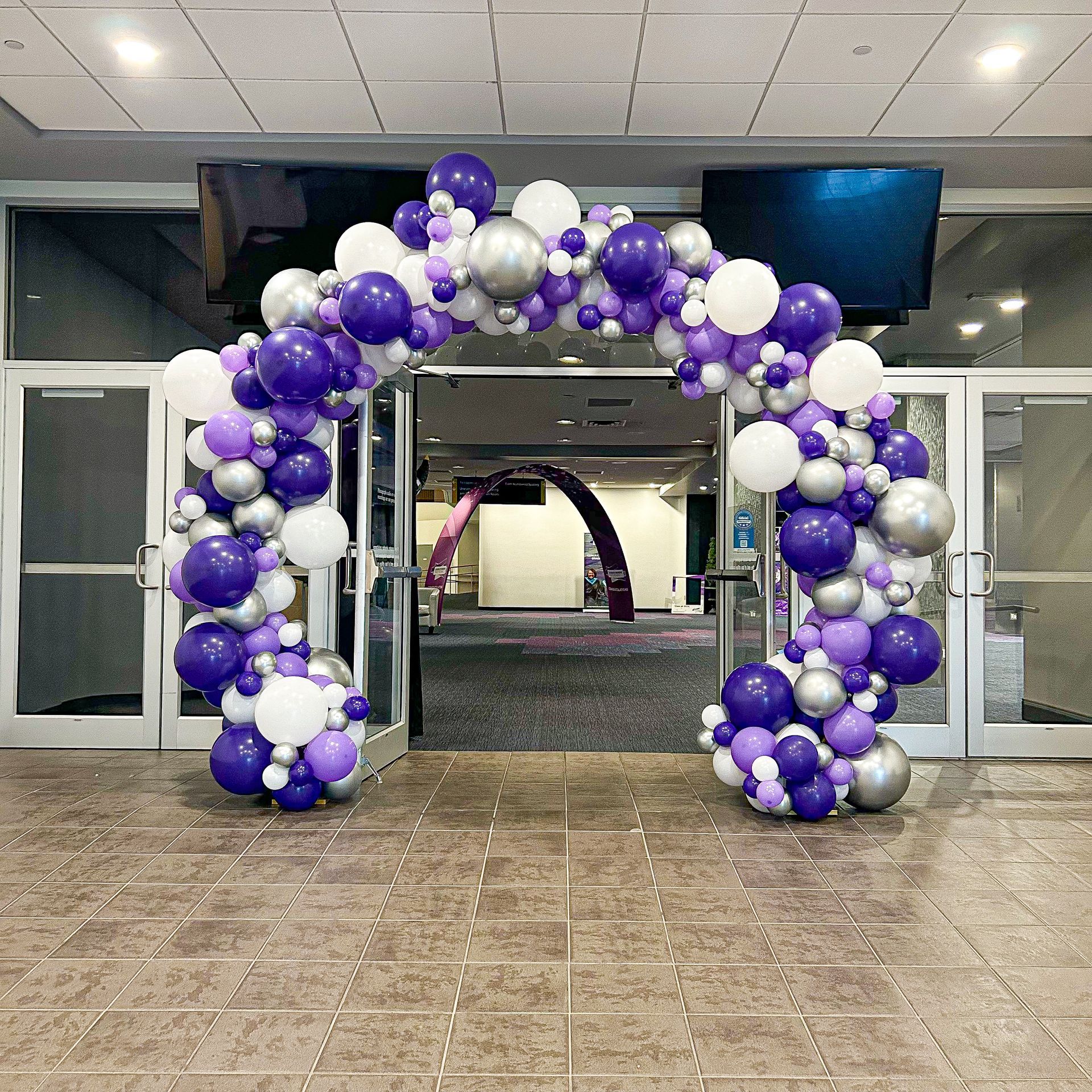 A large arch made of purple , white and silver balloons