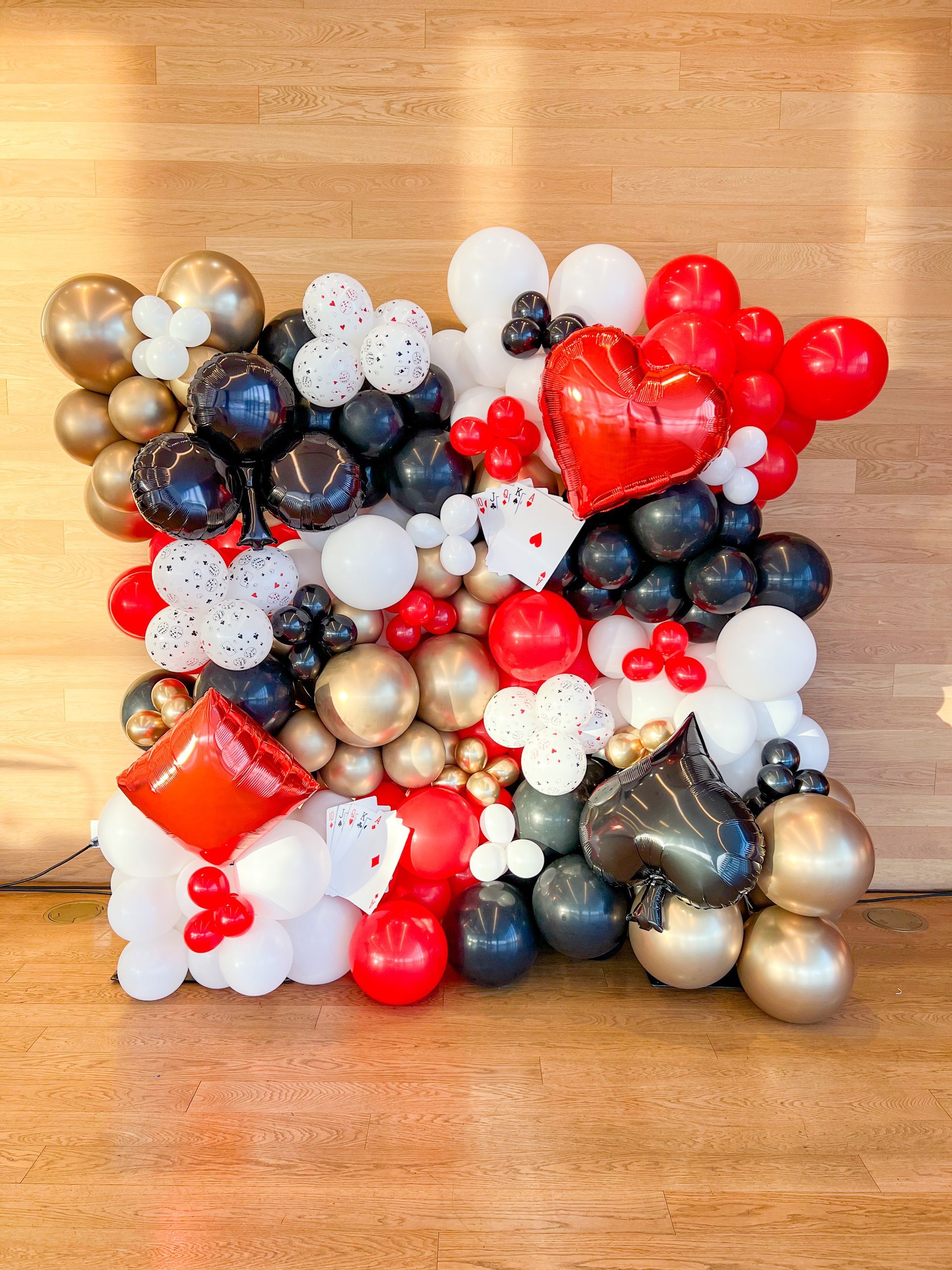 A wall of red , white , black and gold balloons on a wooden floor.