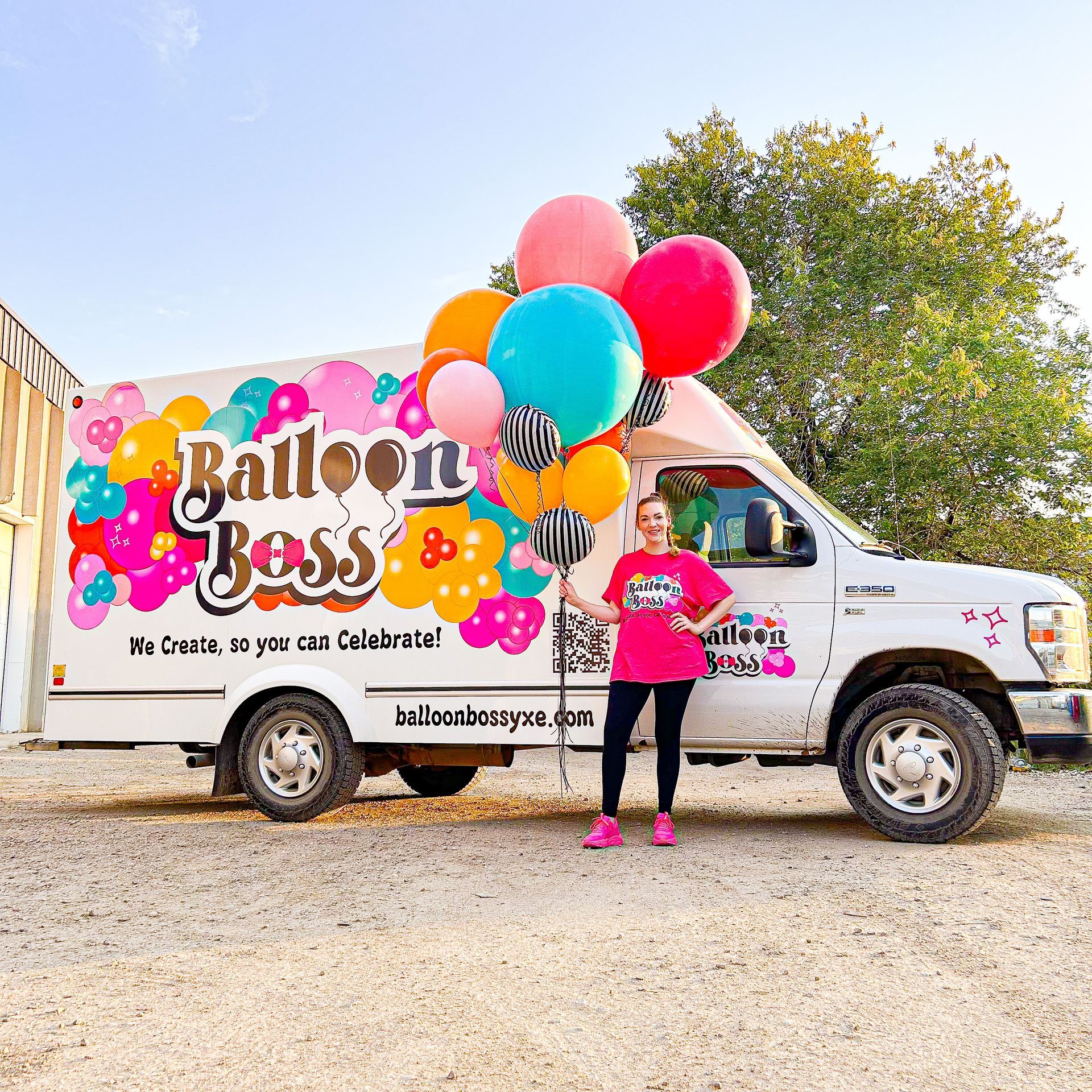 A woman is holding balloons in front of a balloon boss truck.
